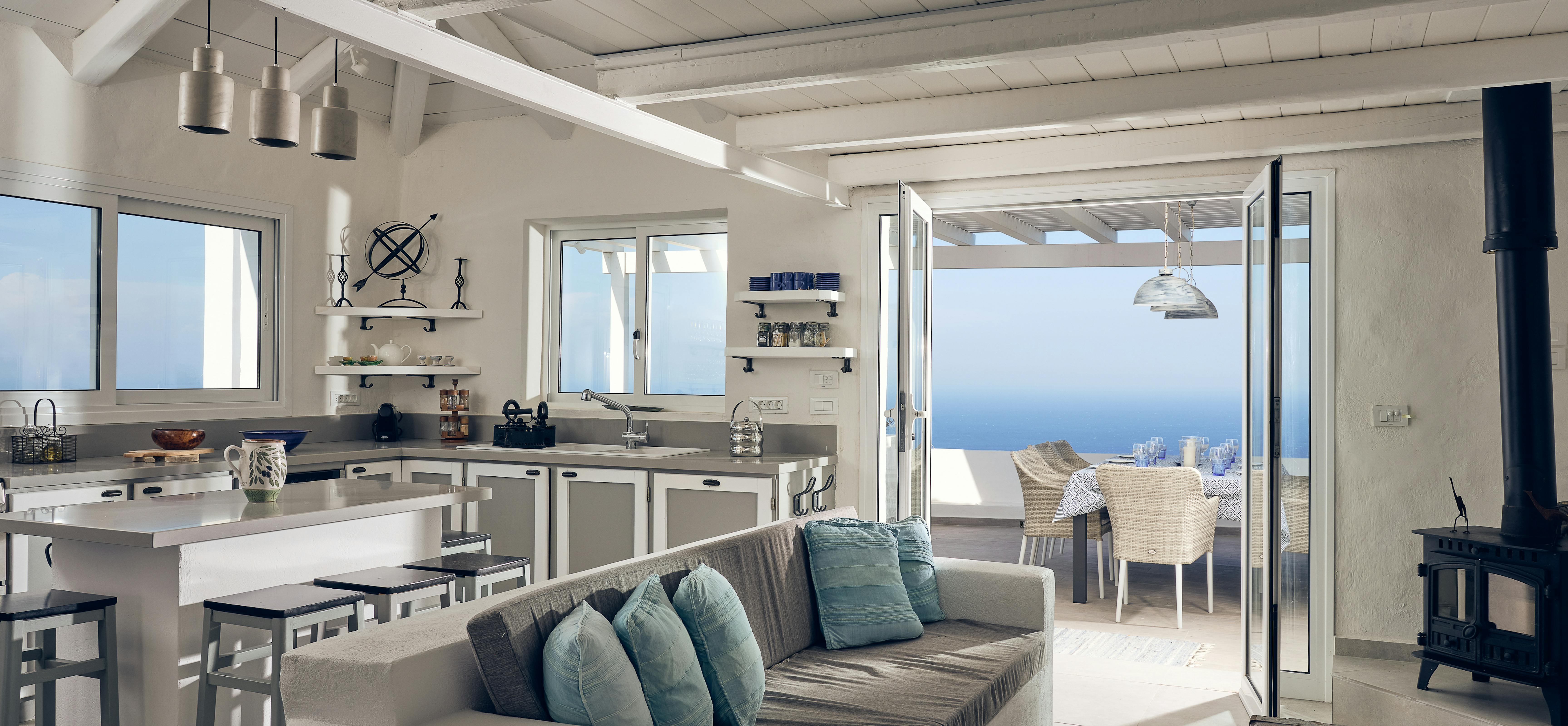 An open-plan living space combines kitchen, dining, and lounge areas with exposed ceiling beams and sea views. The nautical theme continues with rope details and coastal colours throughout the light-filled interior.