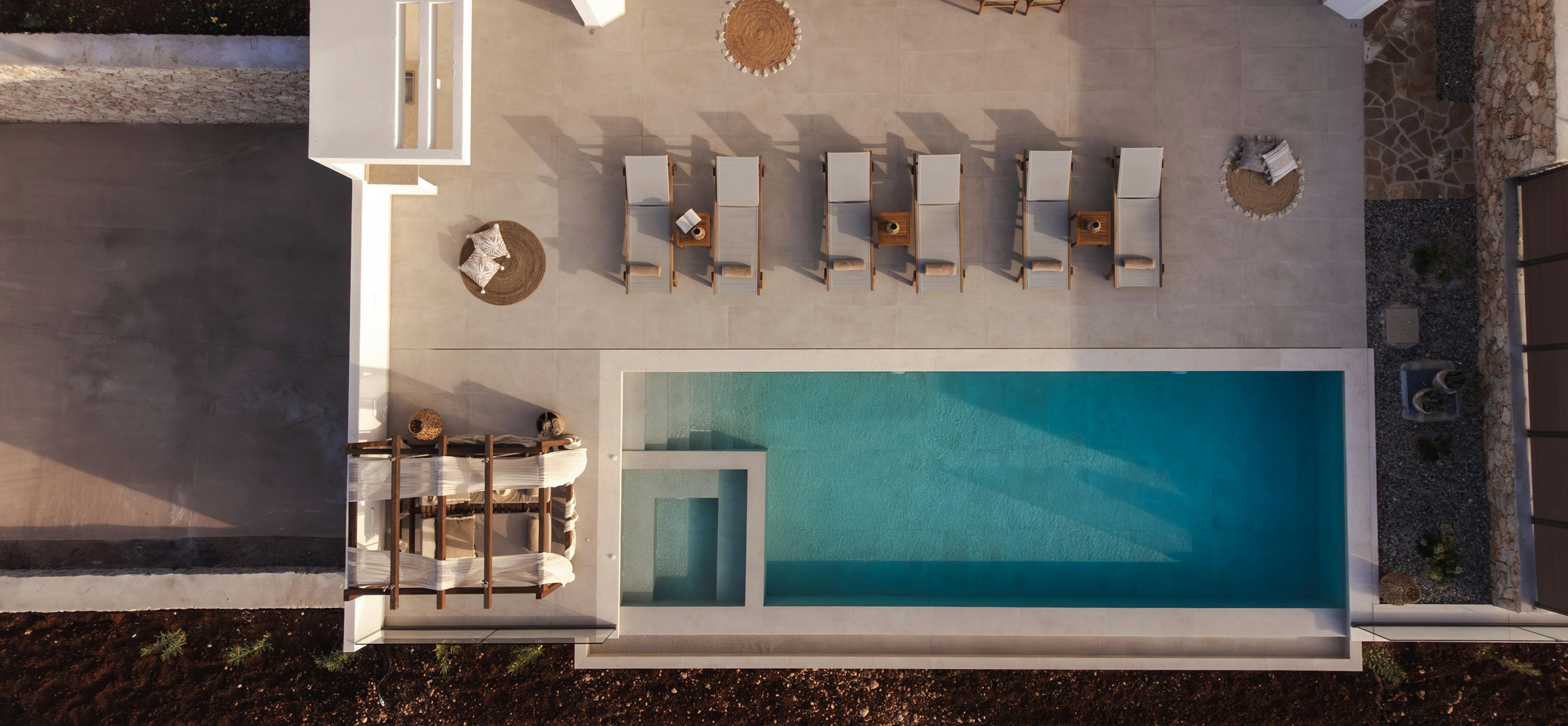 Aerial view of minimalist pool terrace with wooden sun loungers and woven decorative accents.