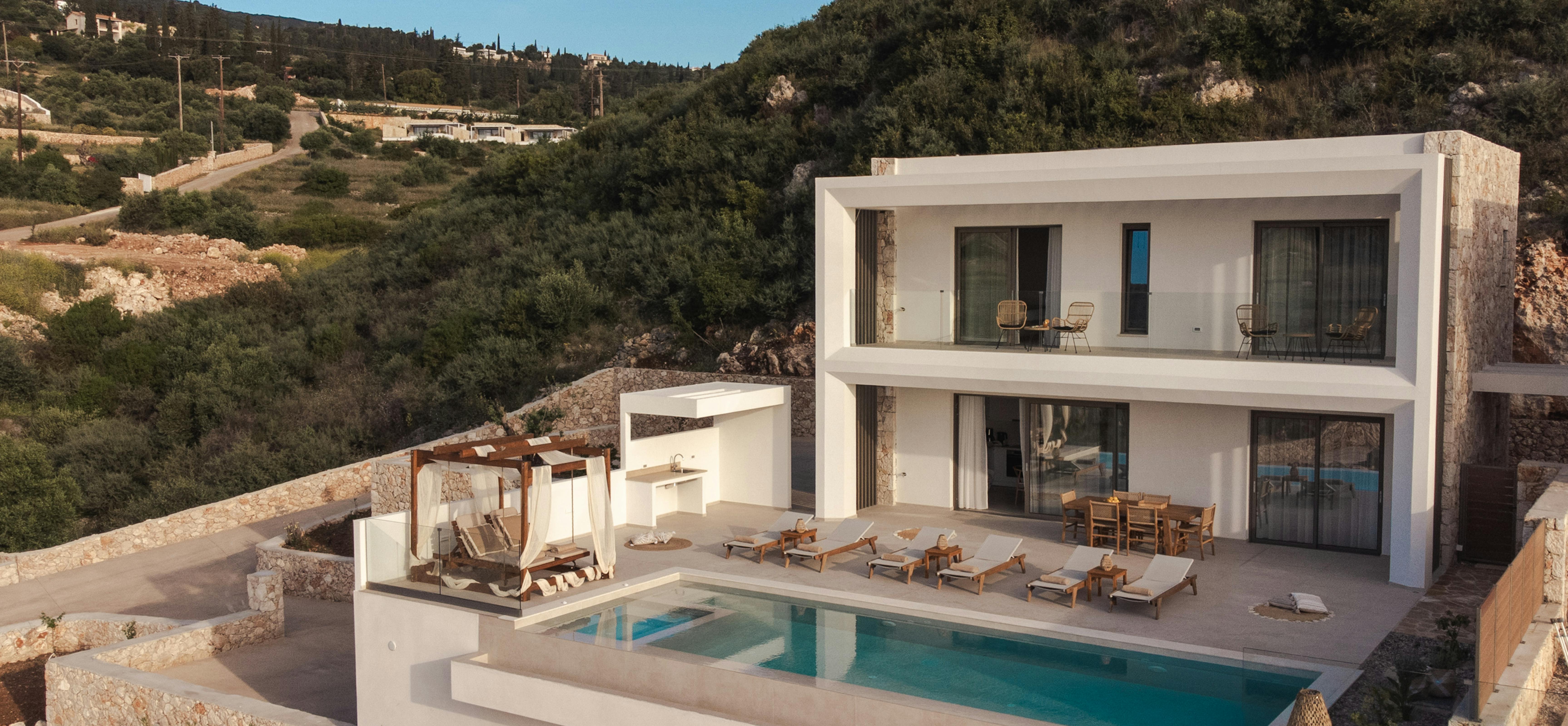 Modern white villa with swimming pool overlooking hillside landscape in Mediterranean setting.