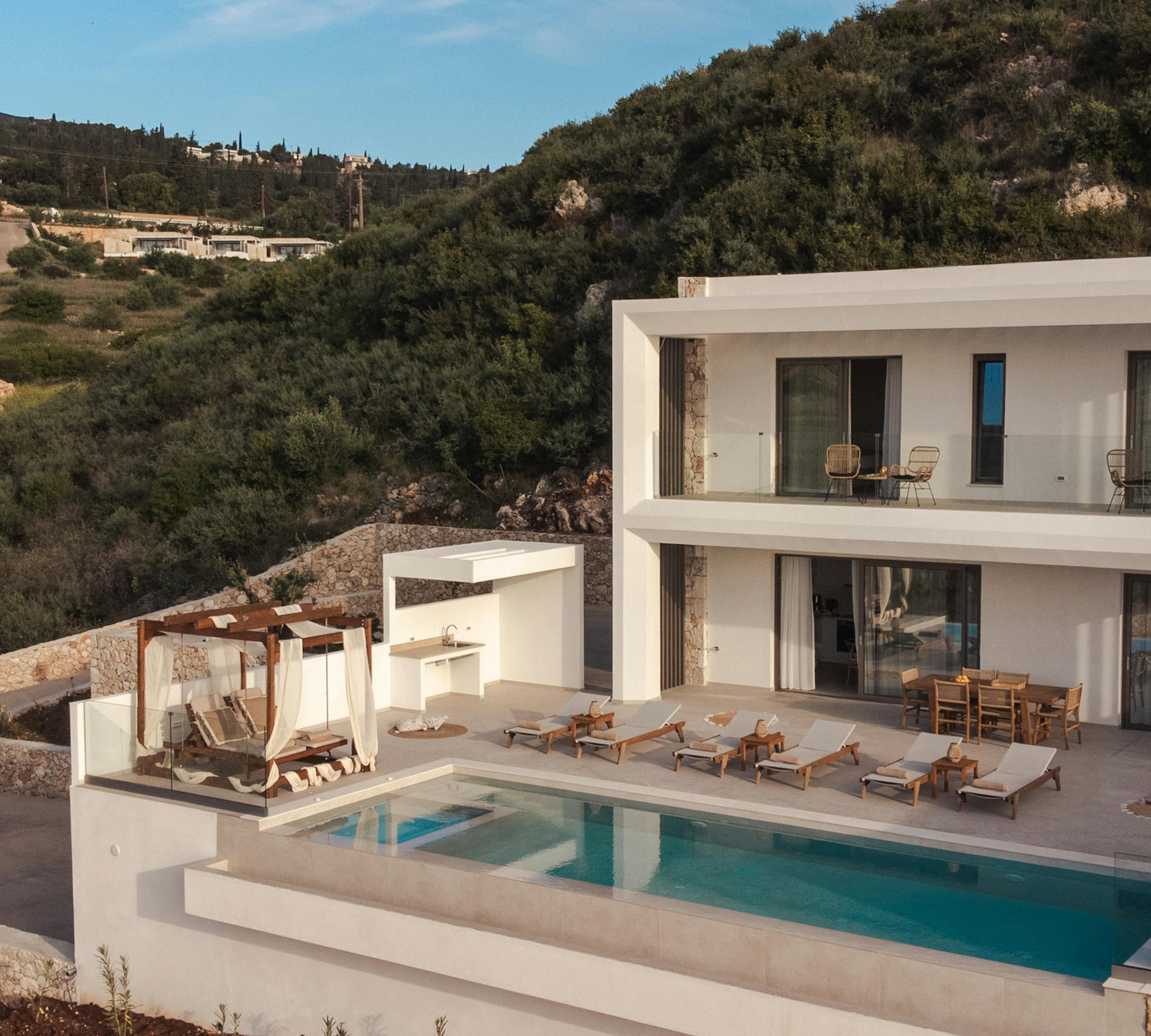 Modern white villa with swimming pool overlooking hillside landscape in Mediterranean setting.