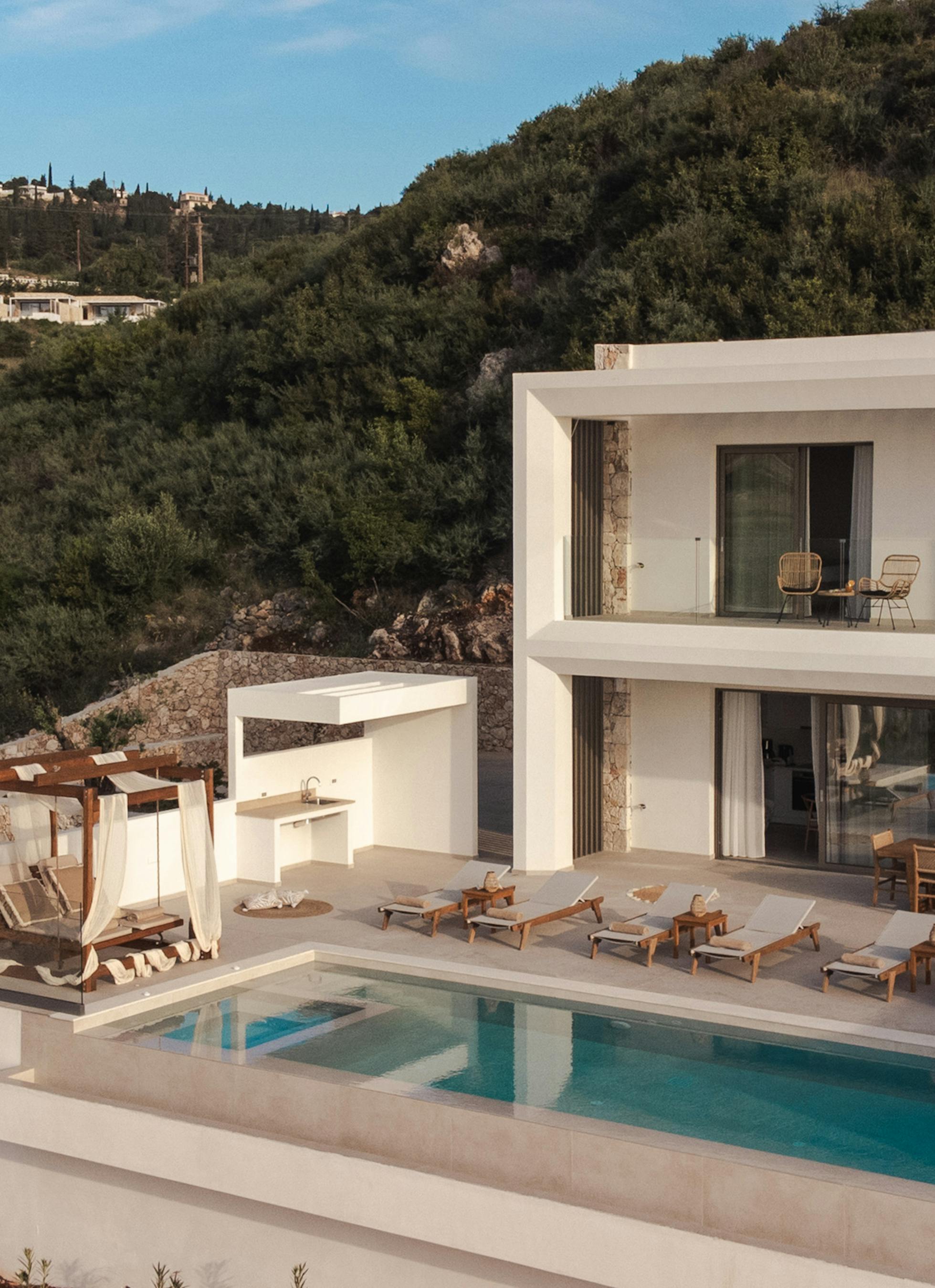 Modern white villa with swimming pool overlooking hillside landscape in Mediterranean setting.