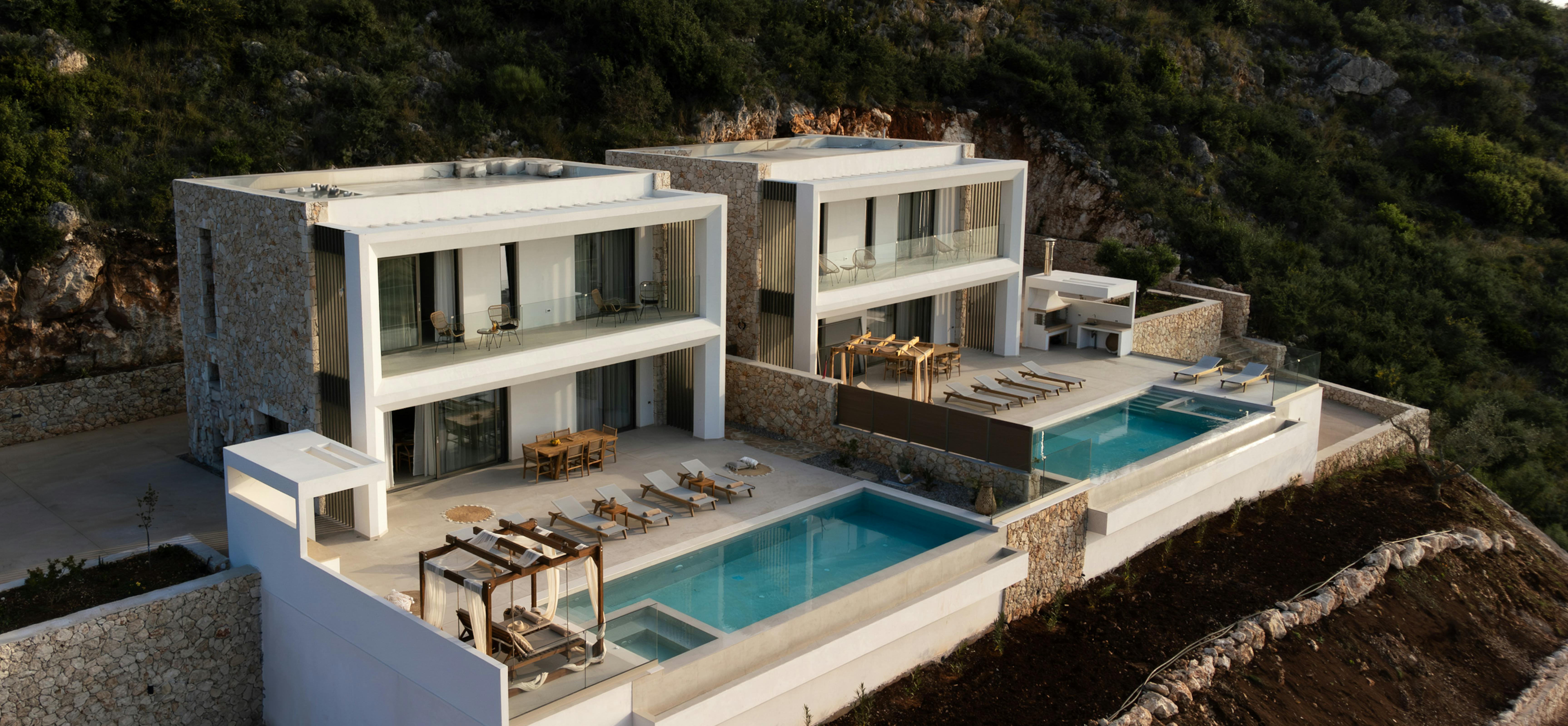 Expansive modern villa complex with multiple pools and terraces carved into hillside.