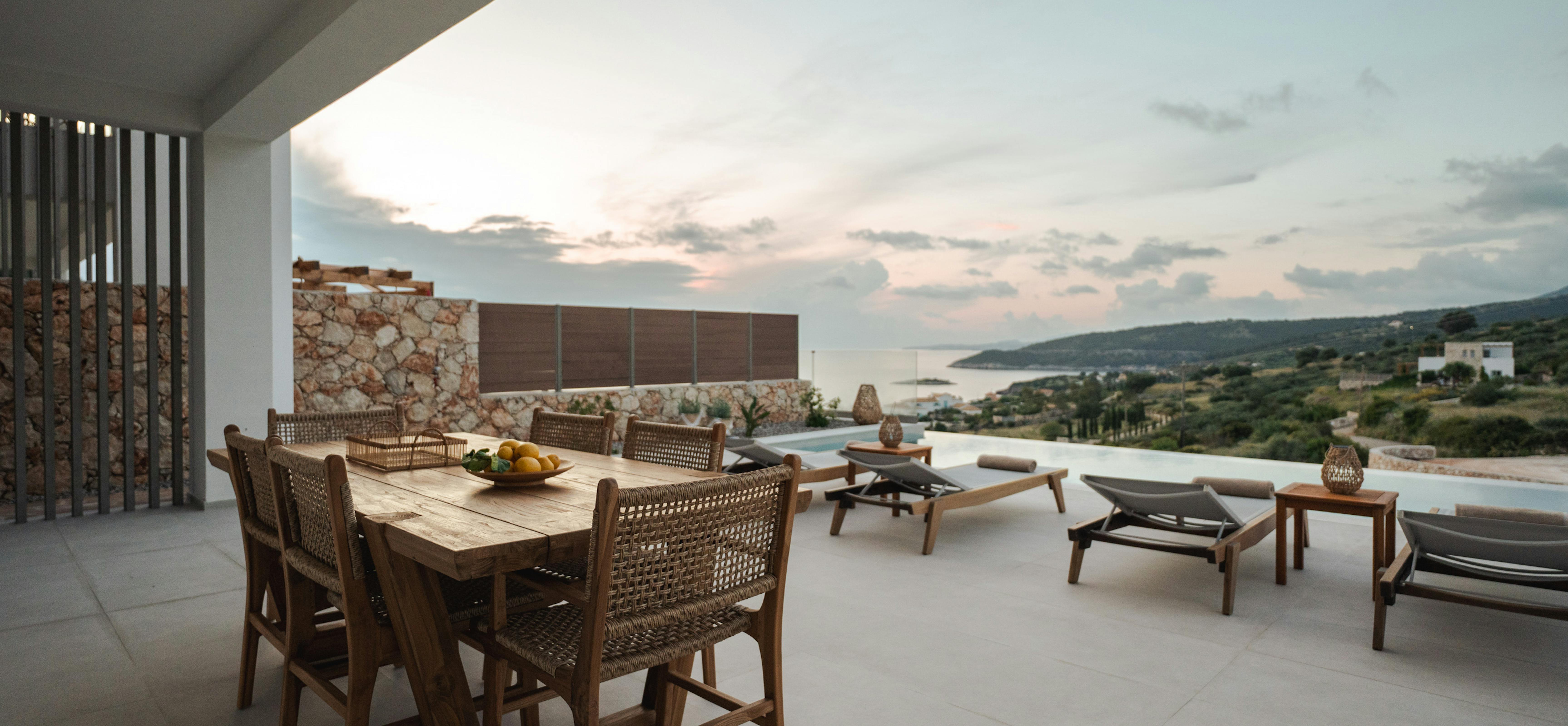 Contemporary outdoor dining area with wicker furniture and panoramic ocean views at dusk.