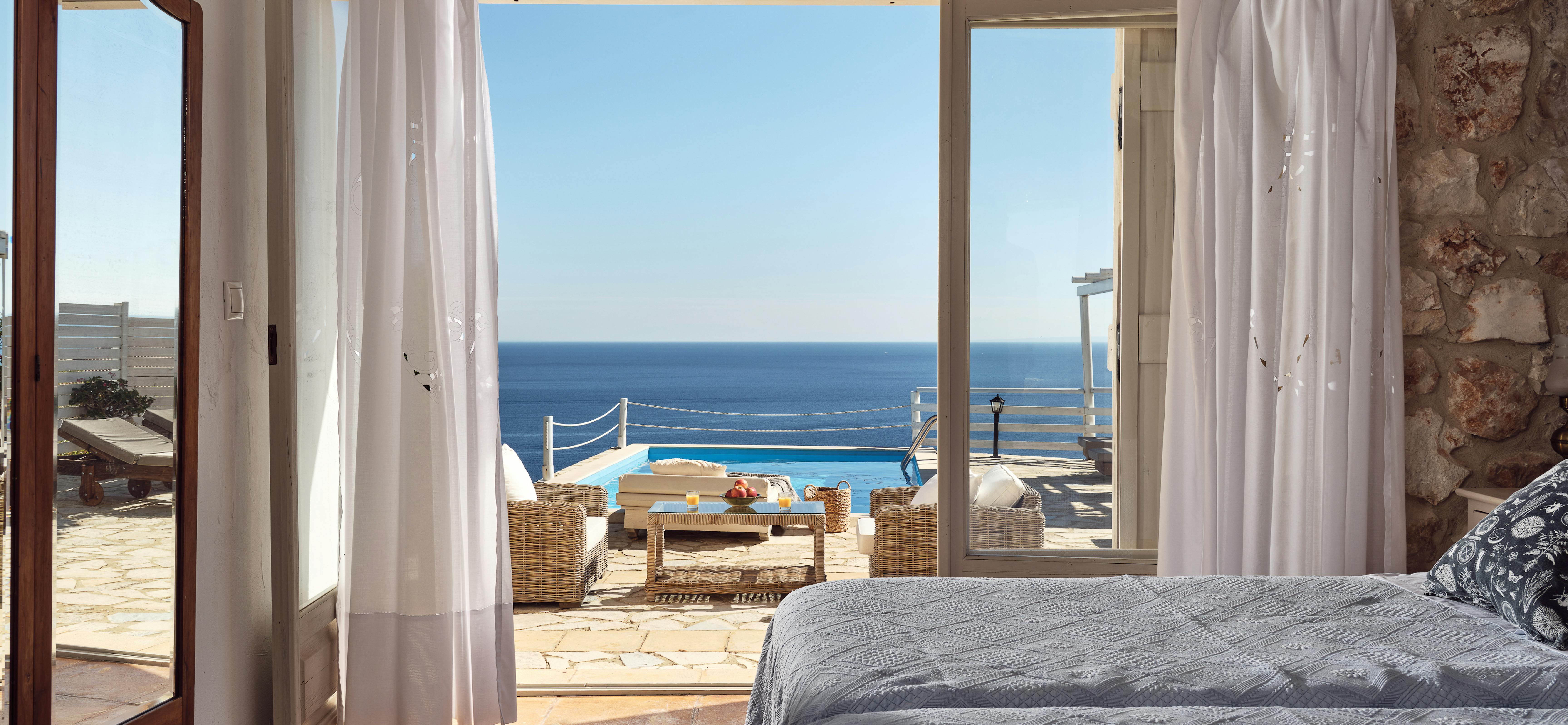 Bedroom with exposed stone walls and sliding glass doors framing pool and ocean views.