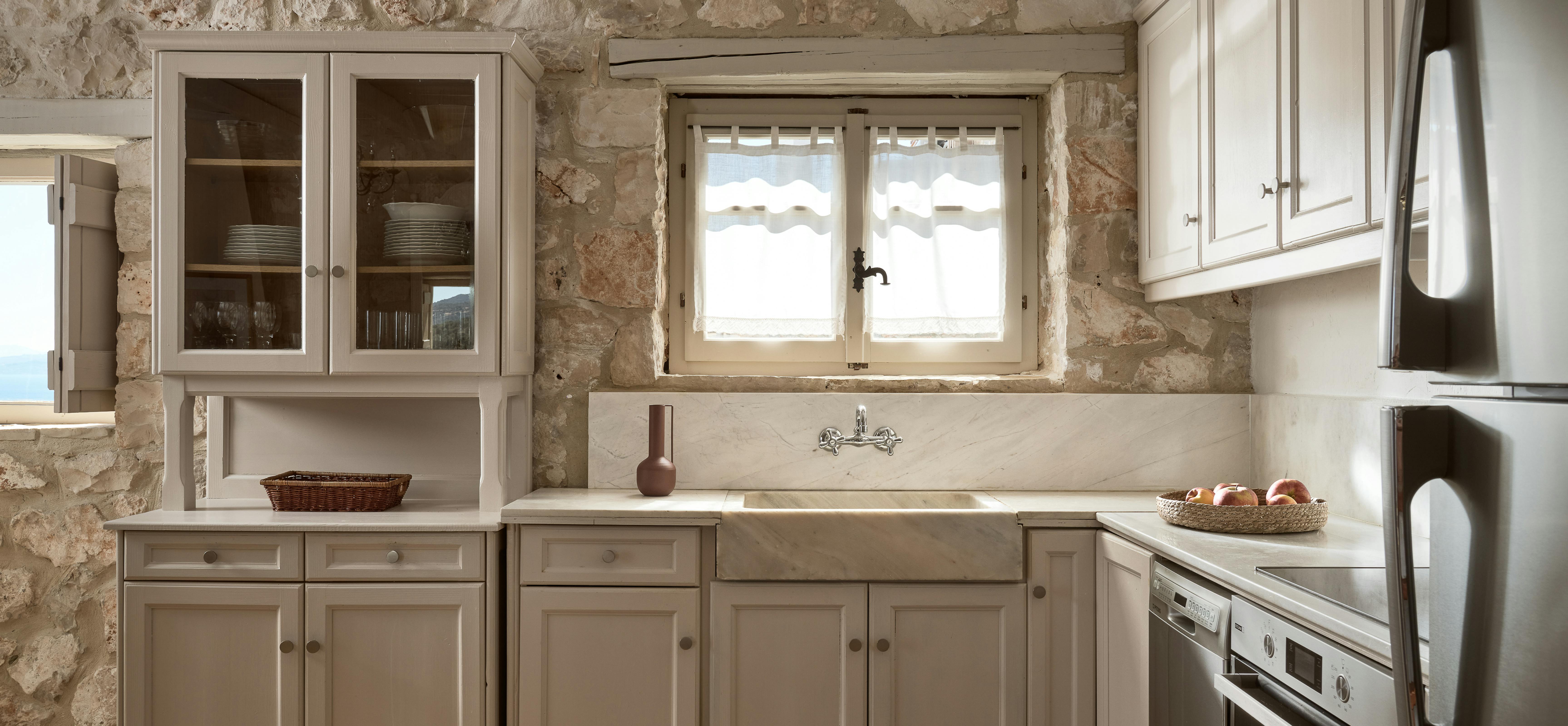 Rustic kitchen with stone walls, cream cabinets, farmhouse sink, and stainless appliances.