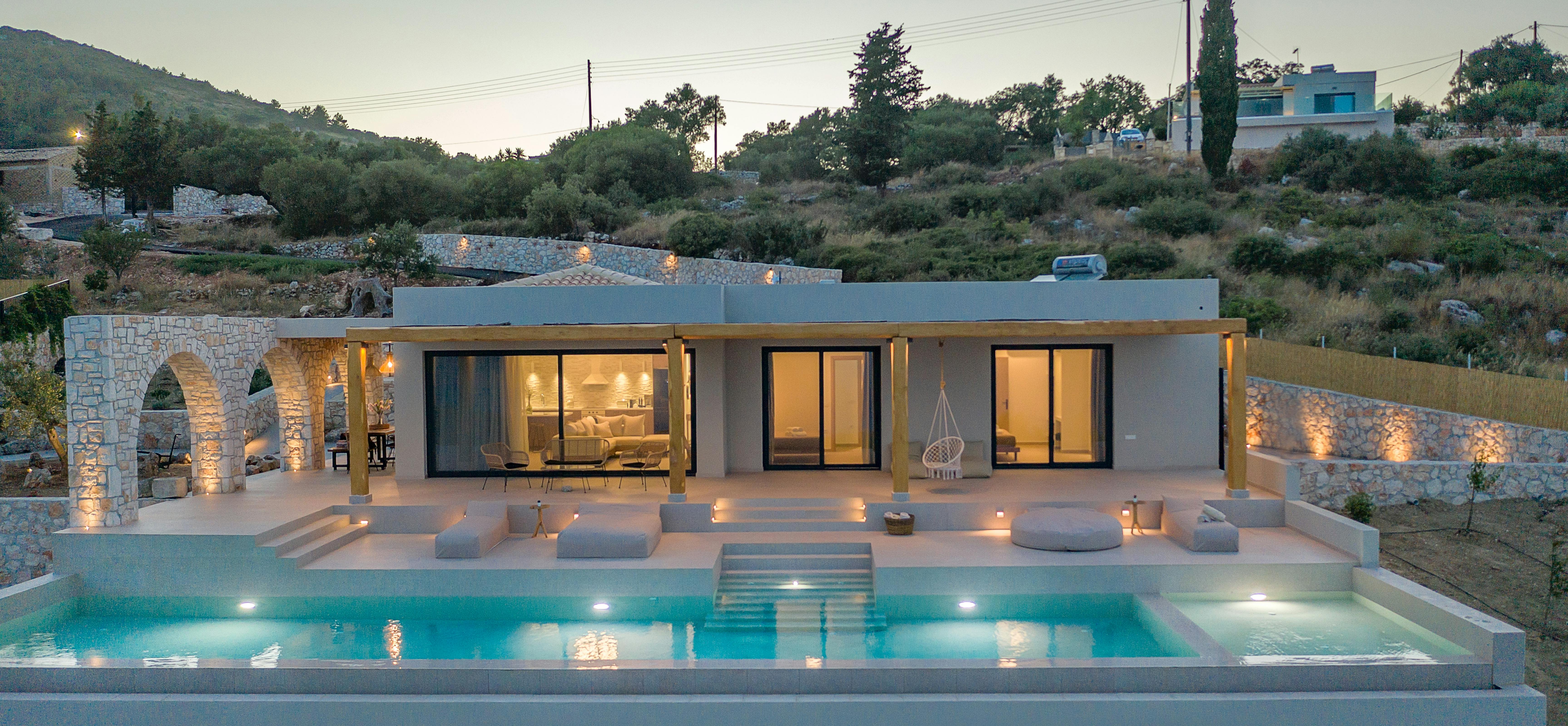 Contemporary hillside villa at twilight with illuminated infinity pool and minimalist lounging terrace.