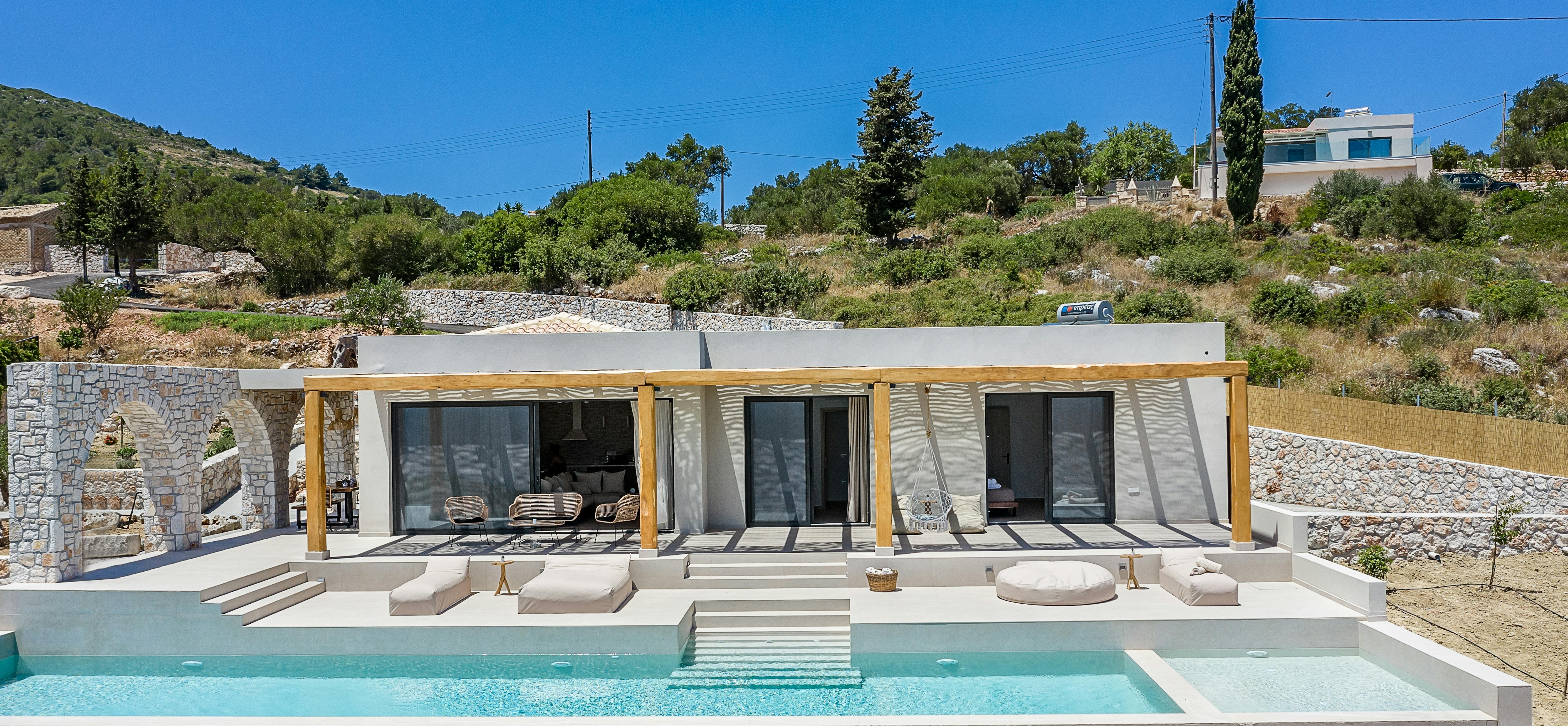 Daytime view of modern villa with multi-level infinity pool and stone retaining walls.