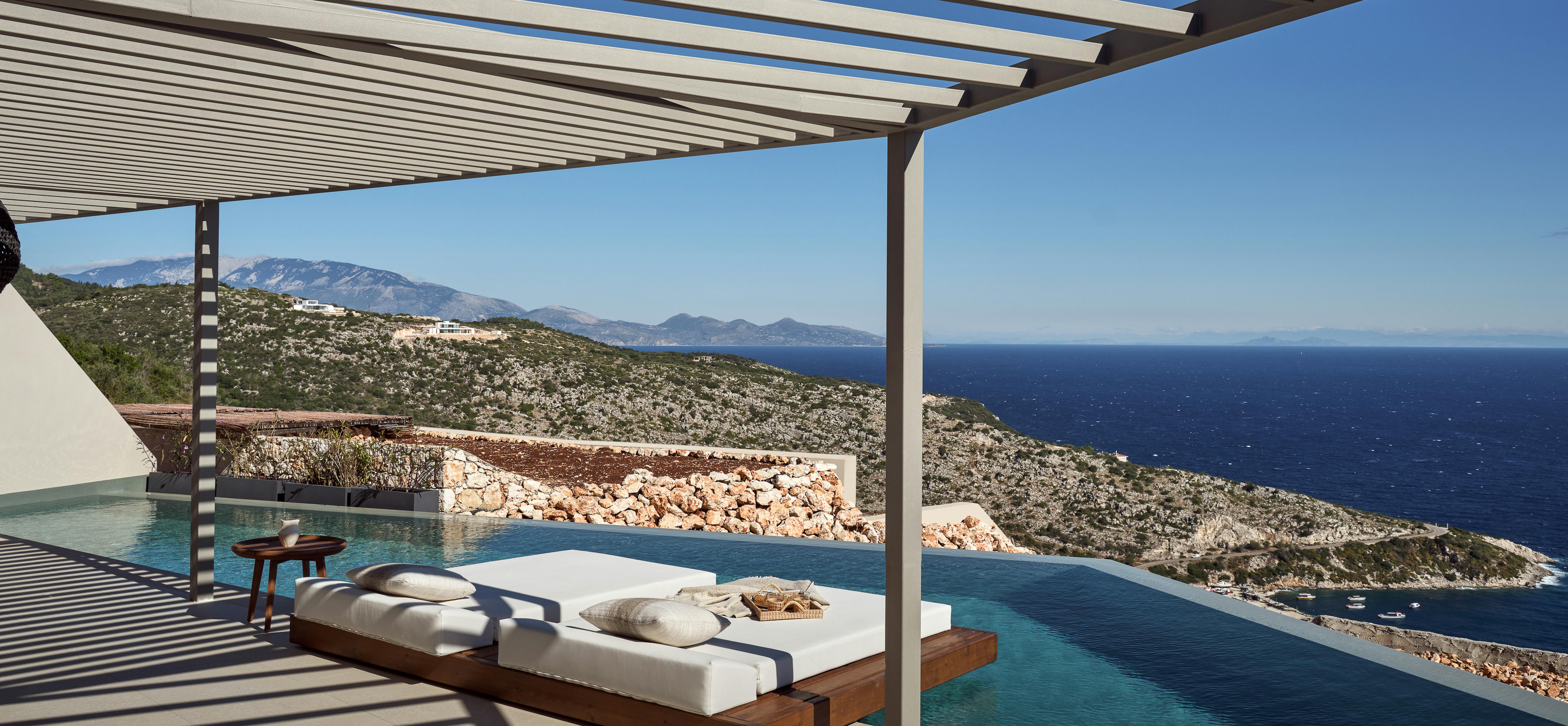 Covered pool terrace with floating daybed overlooking coastal bay and distant mountains.