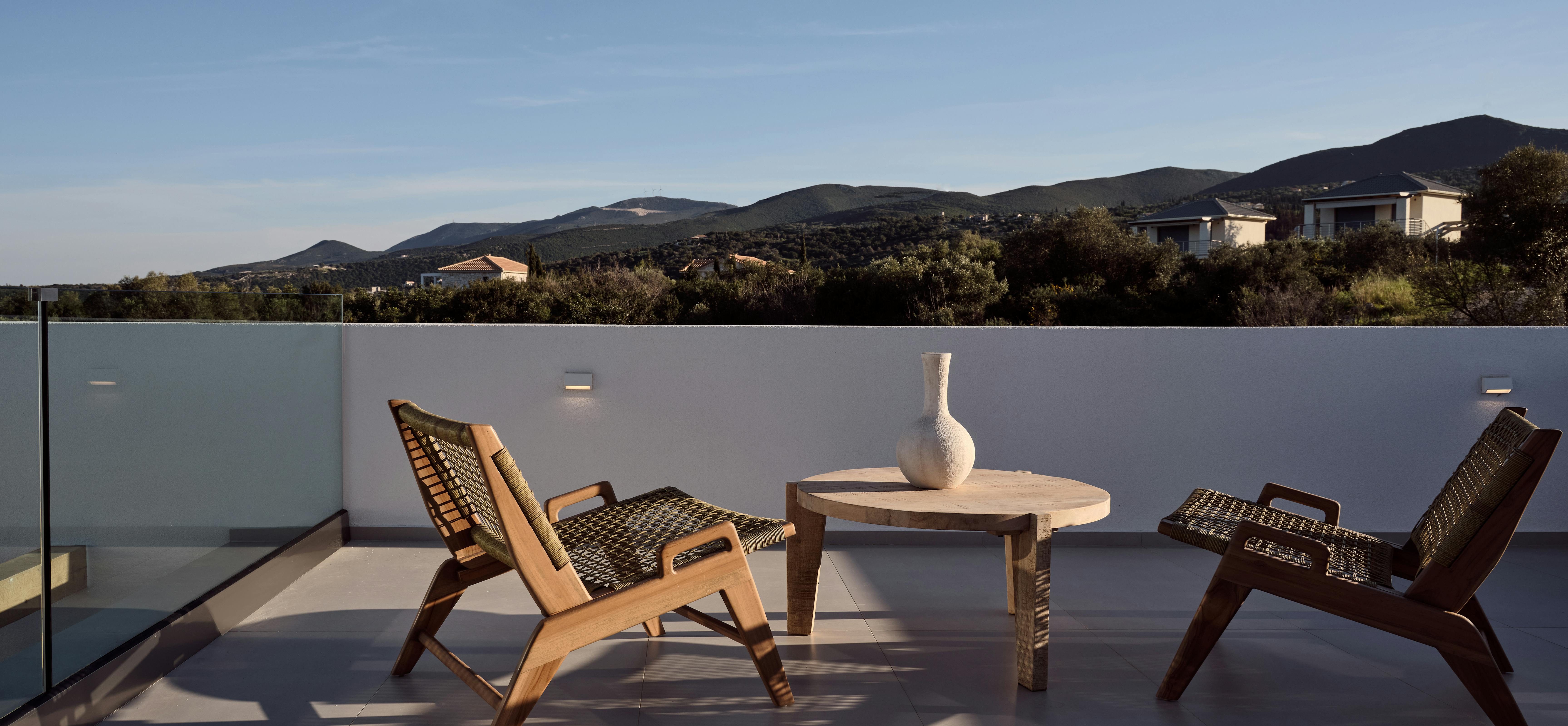 Rooftop terrace with woven lounge chairs, round coffee table, and panoramic mountain landscape views.