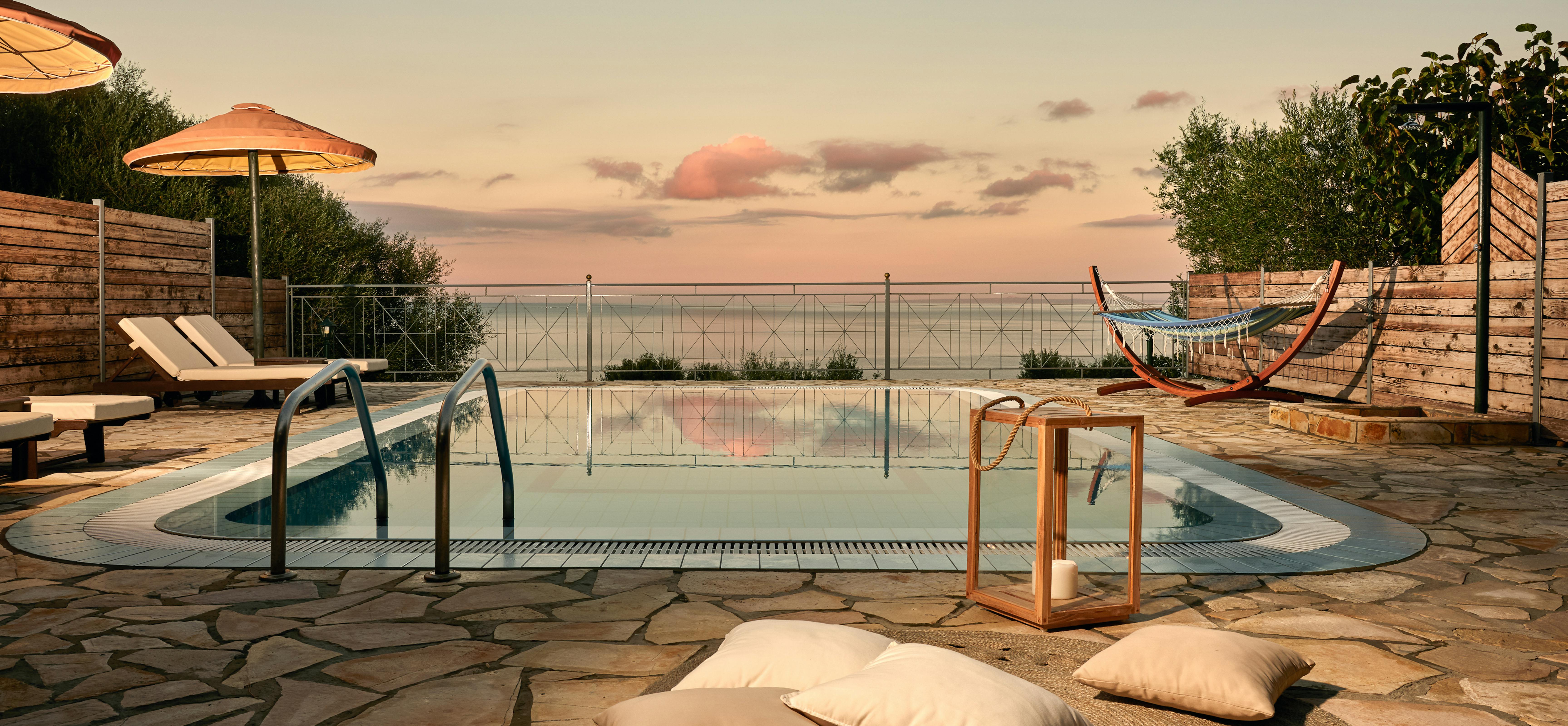 Peaceful pool setting at sunset with hammock and natural stone paving reflecting in still water.