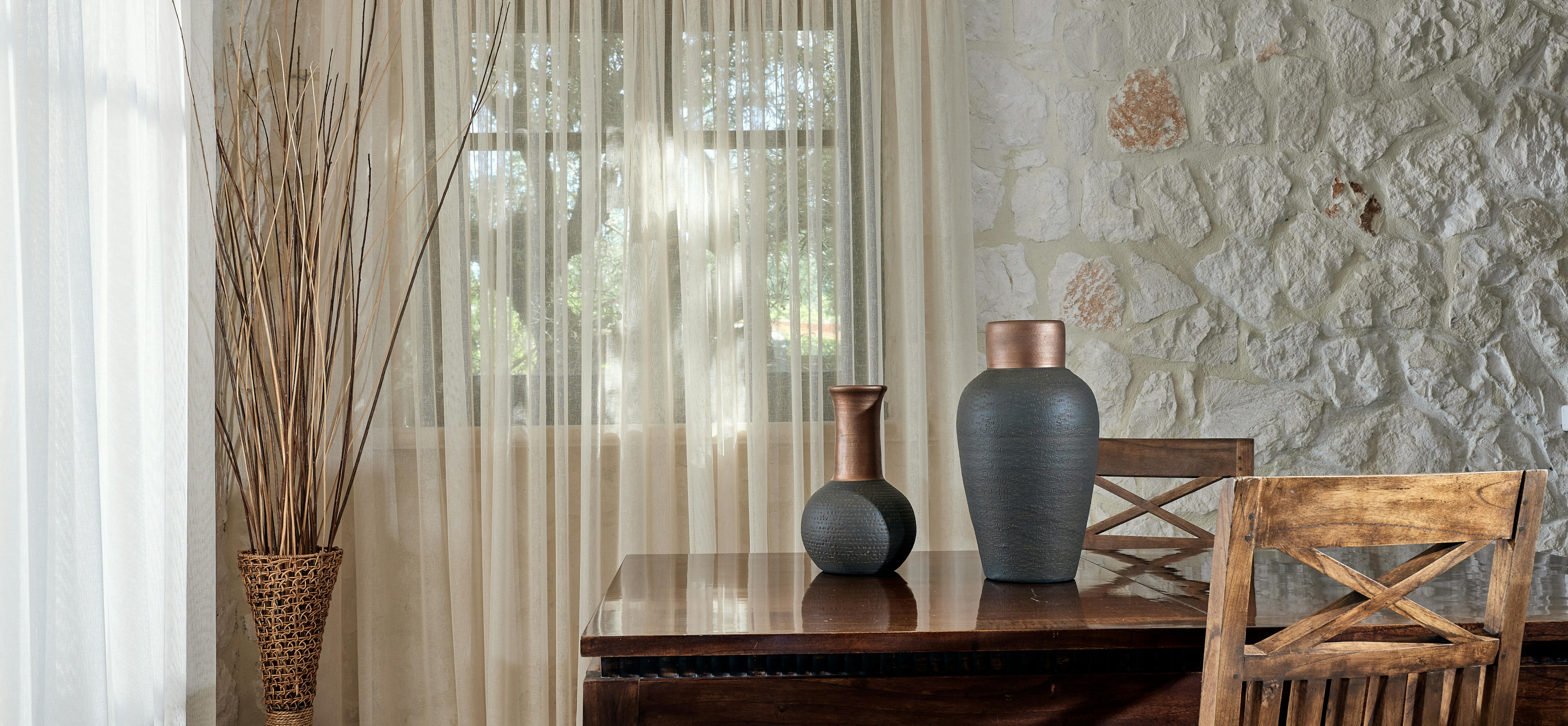 Mediterranean dining area with exposed stone walls, wooden table, and wicker basket containing dried branches.