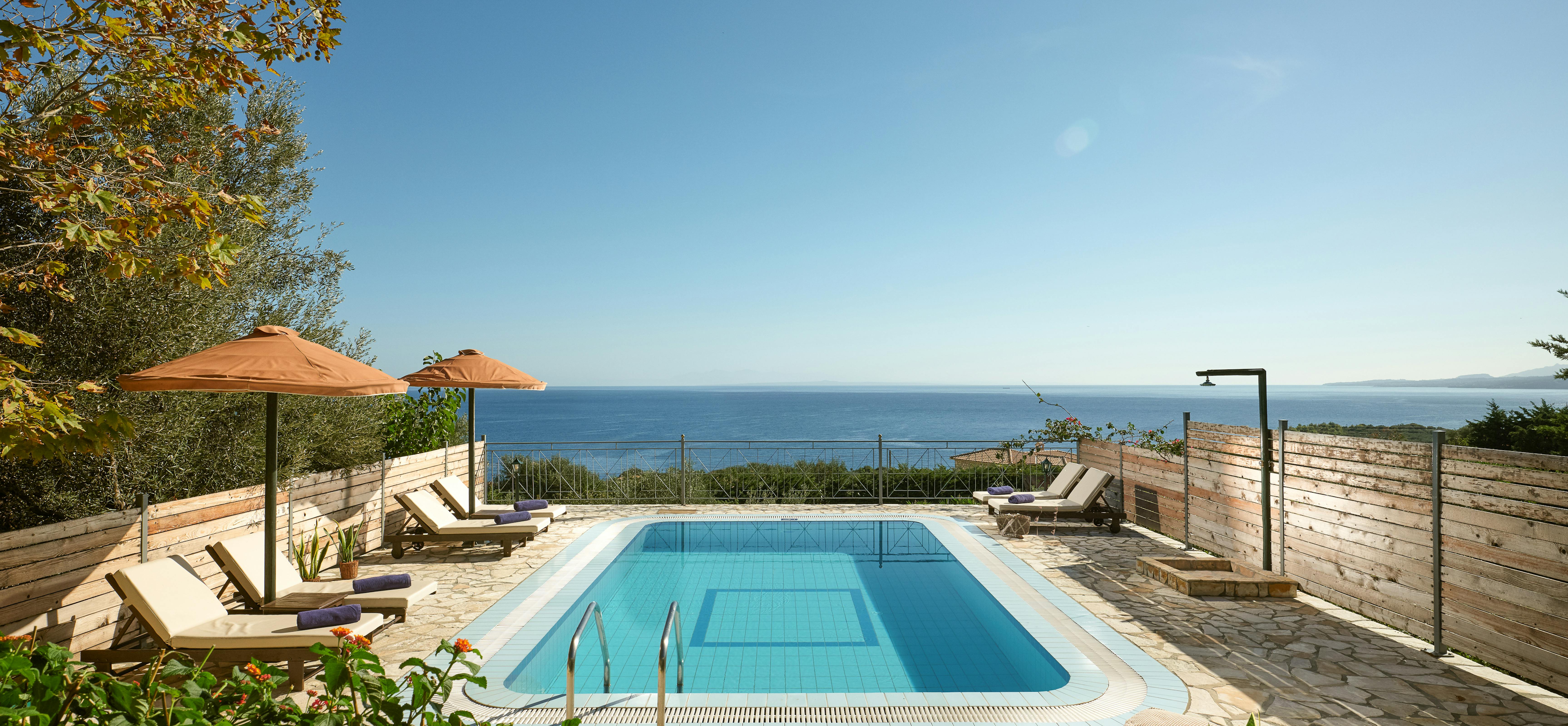 Pool terrace with wooden loungers, umbrellas, and panoramic ocean views beyond privacy fencing.