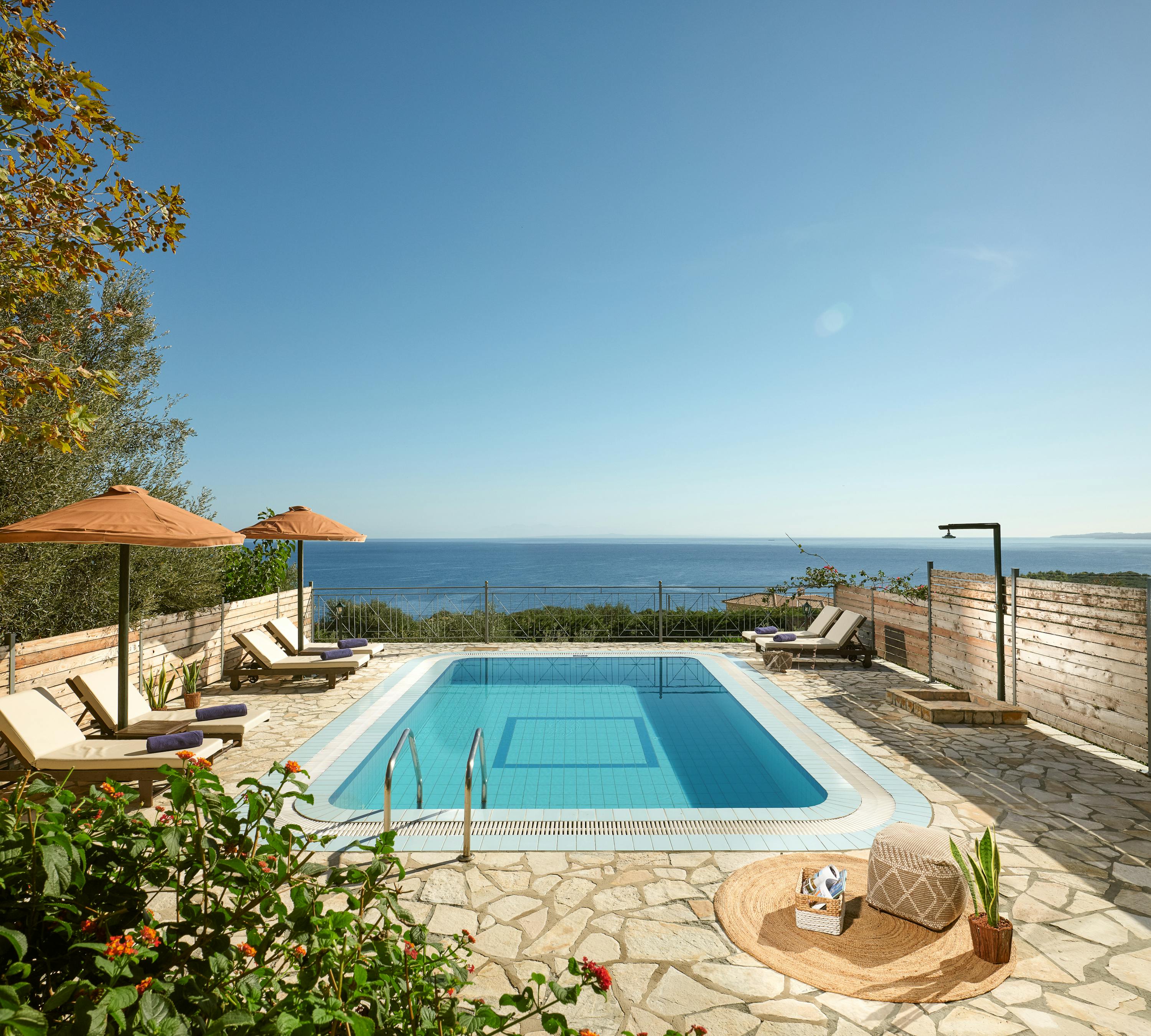 Pool terrace with wooden loungers, umbrellas, and panoramic ocean views beyond privacy fencing.