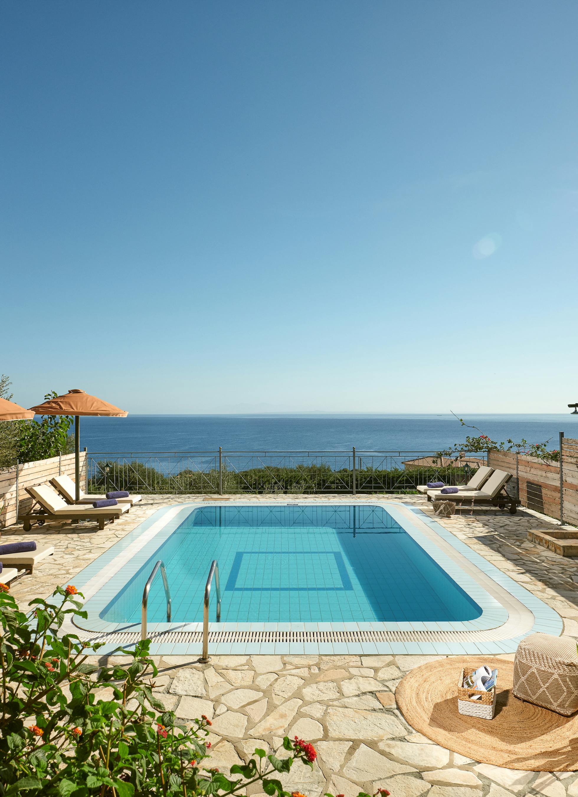 Pool terrace with wooden loungers, umbrellas, and panoramic ocean views beyond privacy fencing.