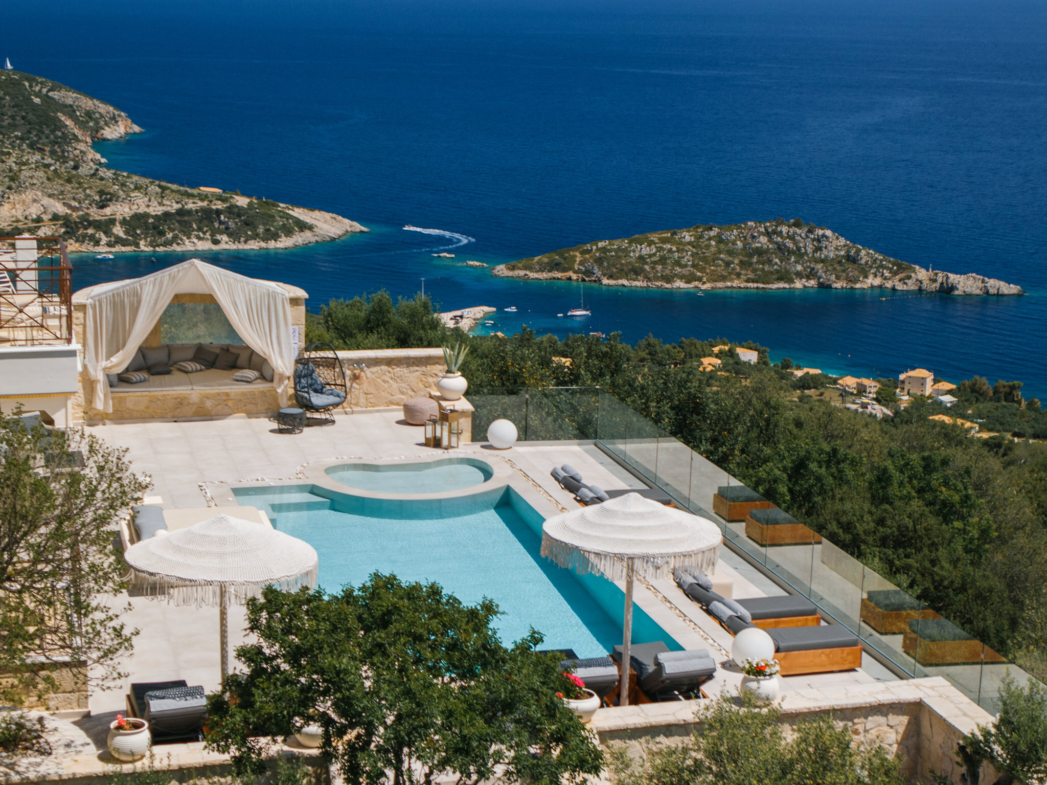 Hillside villa pool terrace overlooking Mediterranean coastline with multiple levels and glass railings.