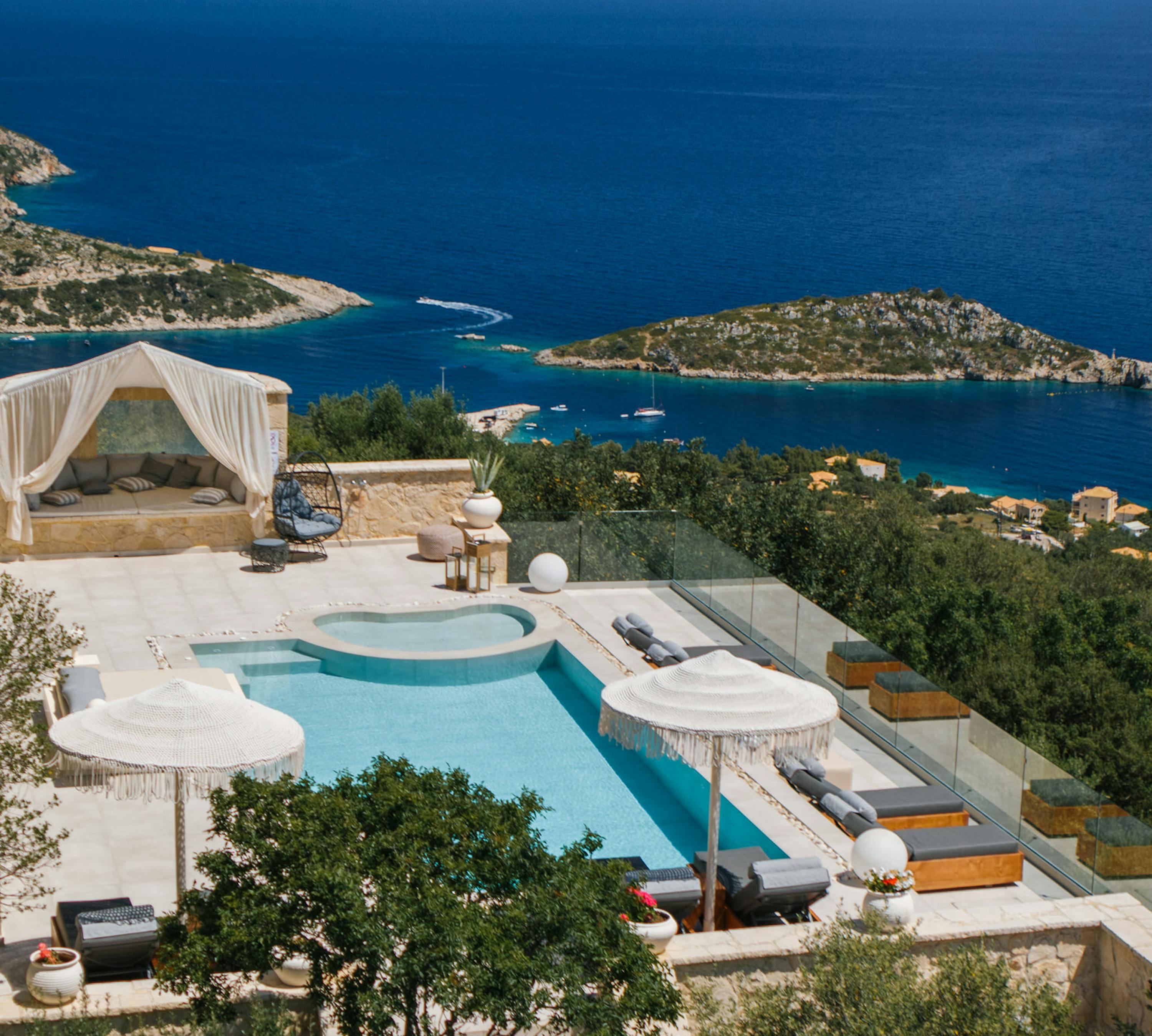 Hillside villa pool terrace overlooking Mediterranean coastline with multiple levels and glass railings.