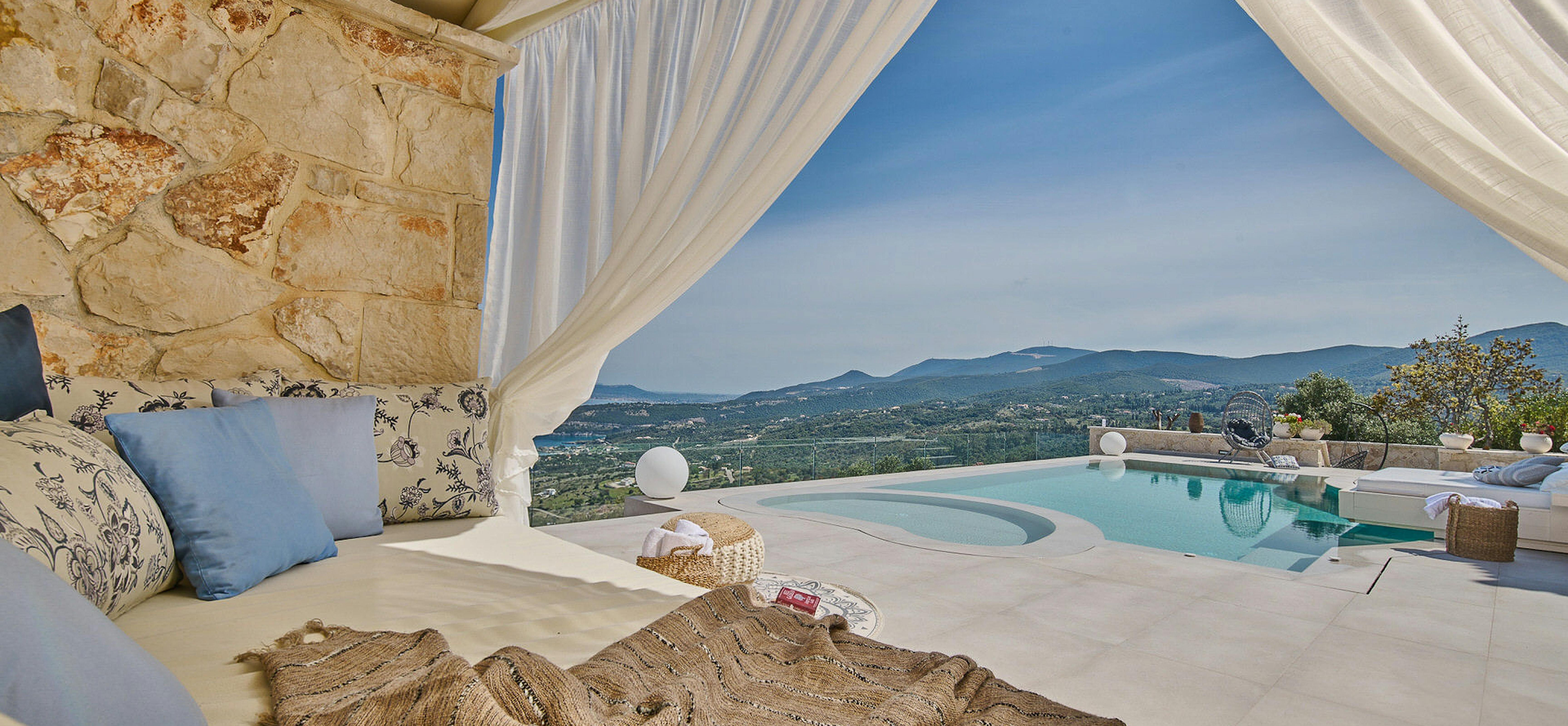 Outdoor daybed with flowing curtains overlooking infinity pool and distant mountain ranges.