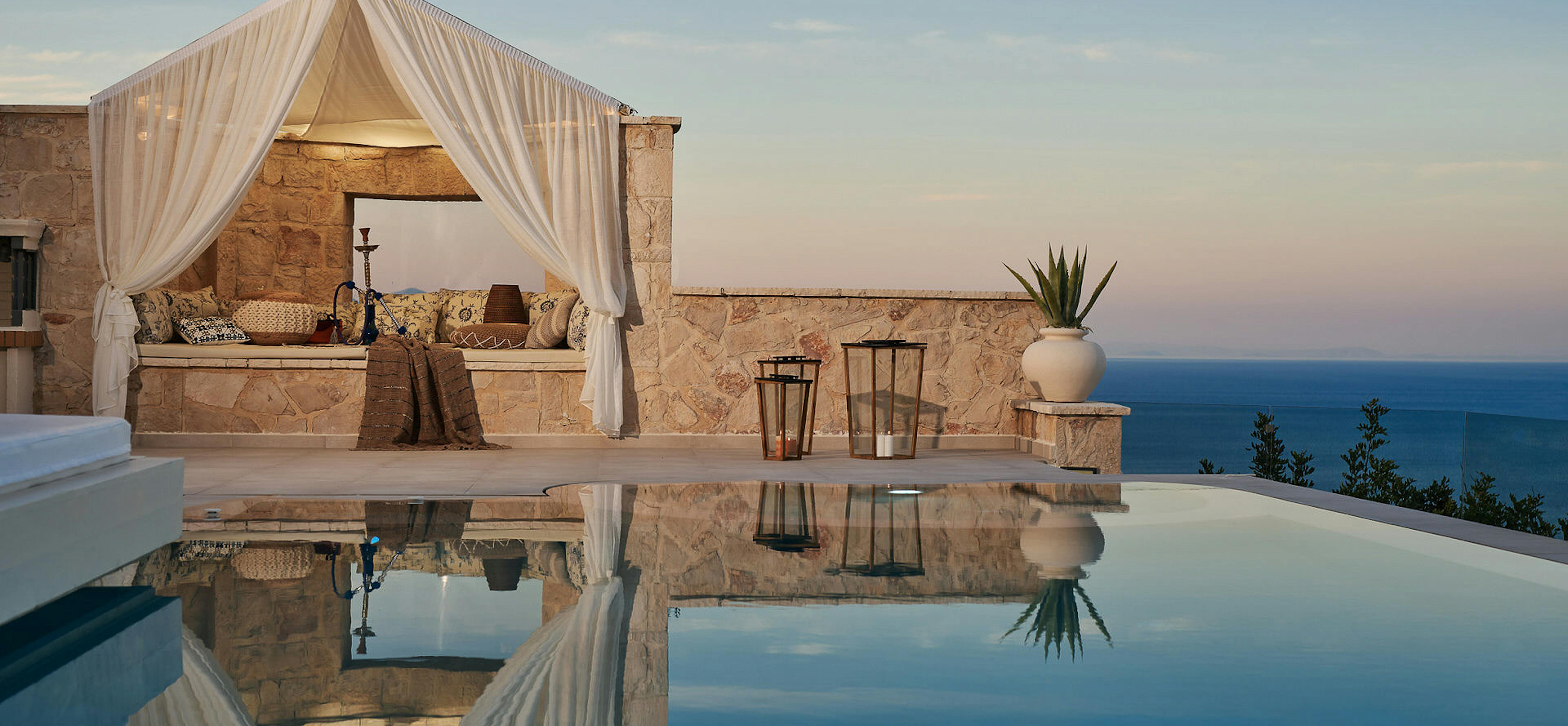 Evening infinity pool scene with stone cabana and perfect reflections of sky and architecture.