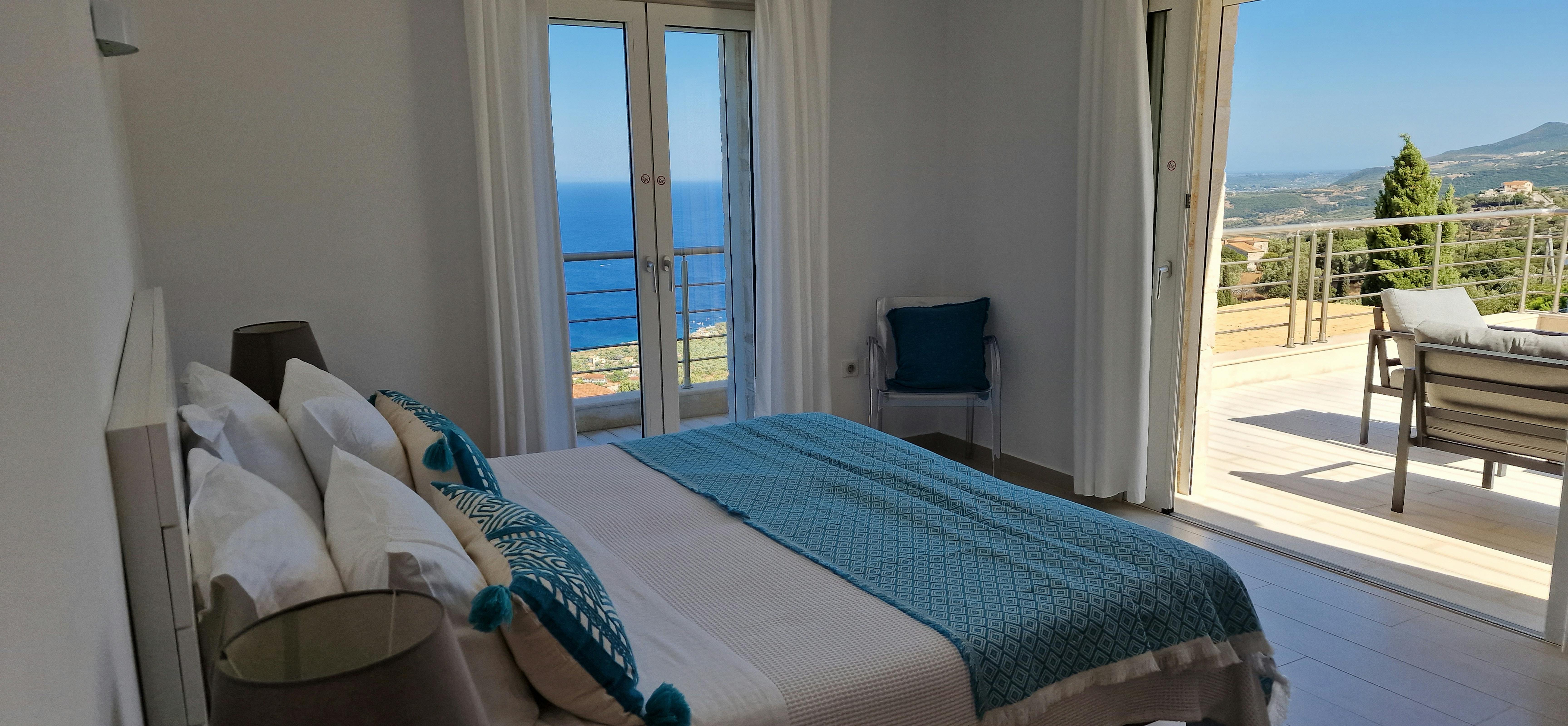 Master bedroom with teal accents, French doors to terrace, and sweeping coastal panorama.