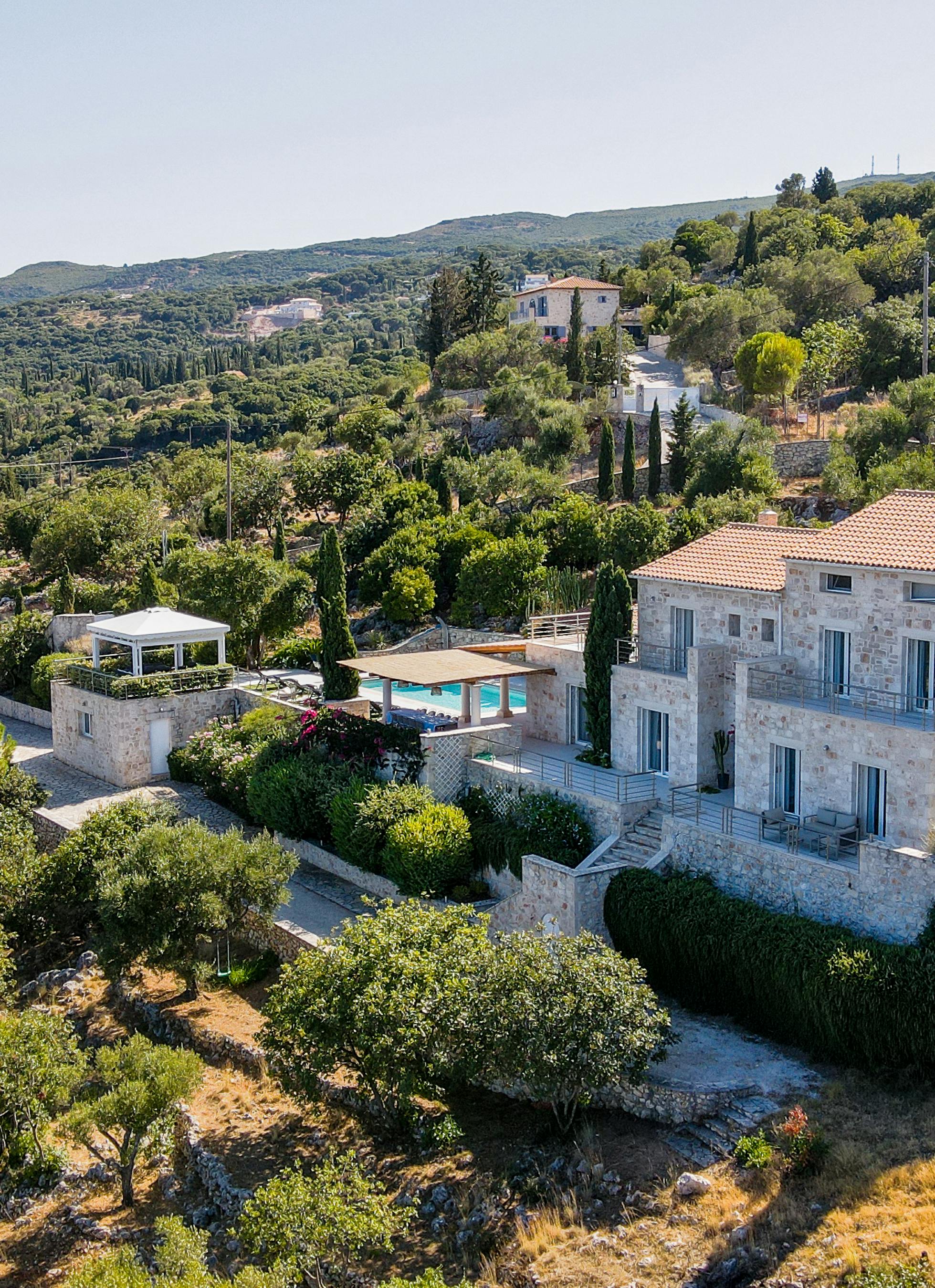 Aerial view of Mediterranean stone villa with terracotta roofs nestled in lush hillside landscape.