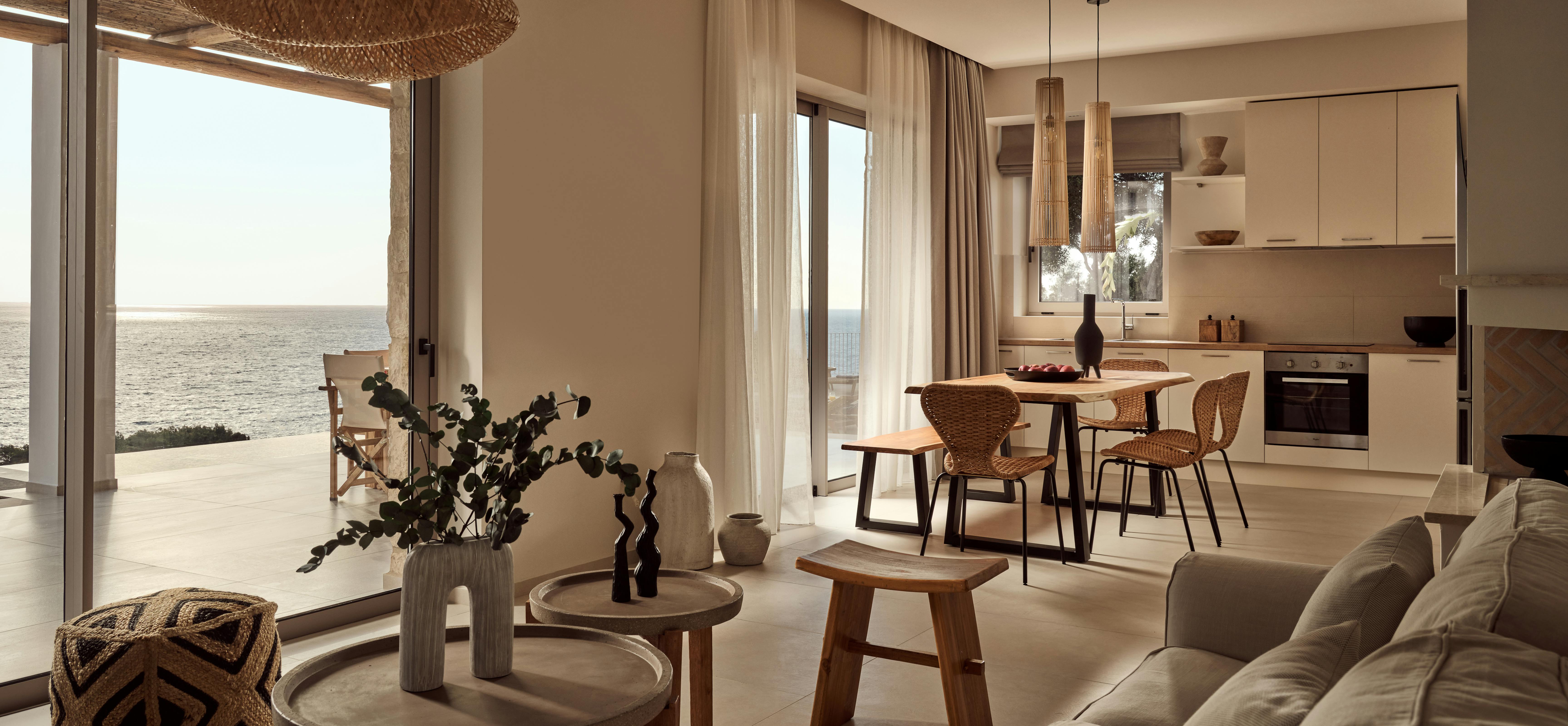 Open-plan living space with natural materials, featuring woven pendant light, wooden dining furniture, and floor-to-ceiling windows with sea views.