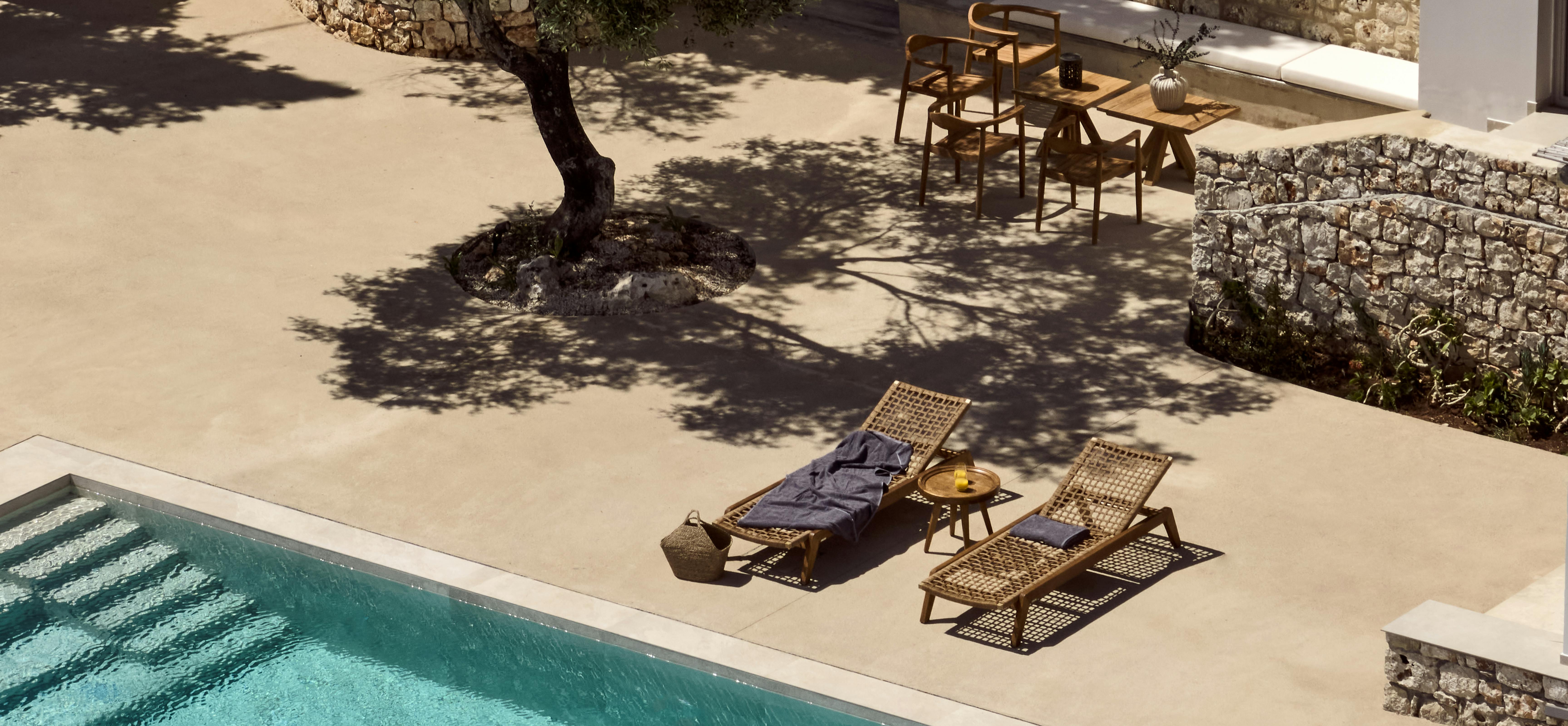 Aerial view of rectangular pool with woven loungers, preserved olive tree, and stone terrace walls integrated into landscape.