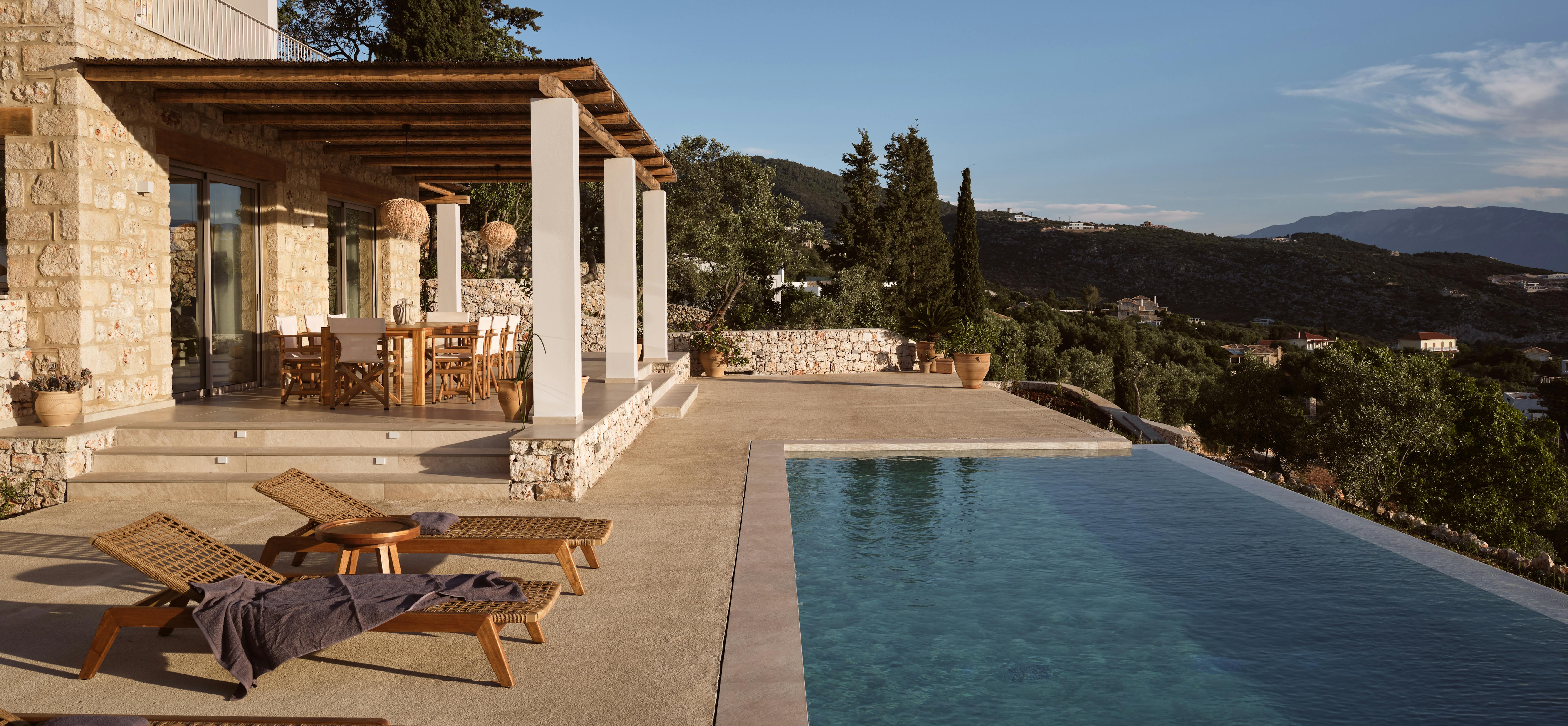 Pool terrace at dusk with infinity edge, traditional reed pergola, and mountain coastline visible across the water.