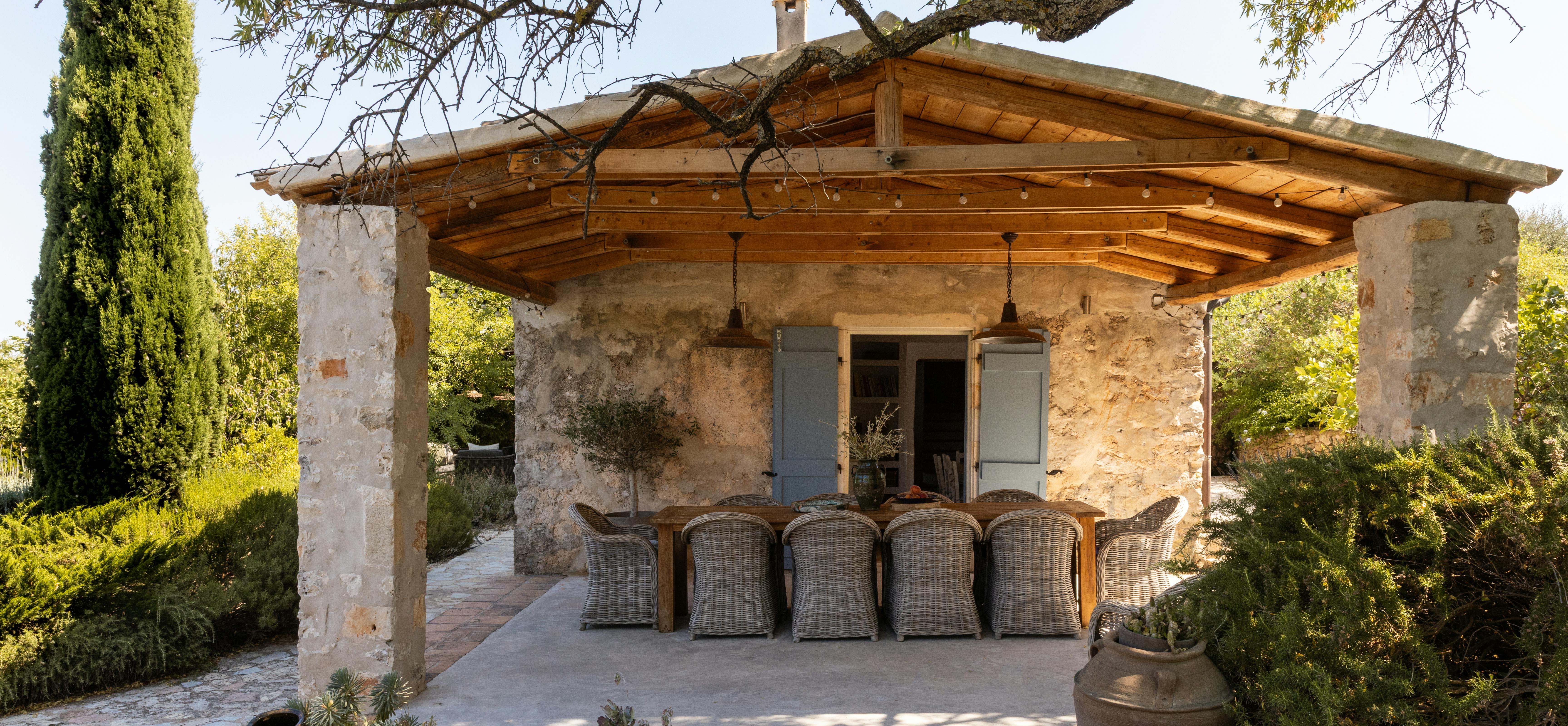 Outdoor dining pergola with rustic stone walls, woven chairs, and ancient olive tree providing natural shade over terrace.