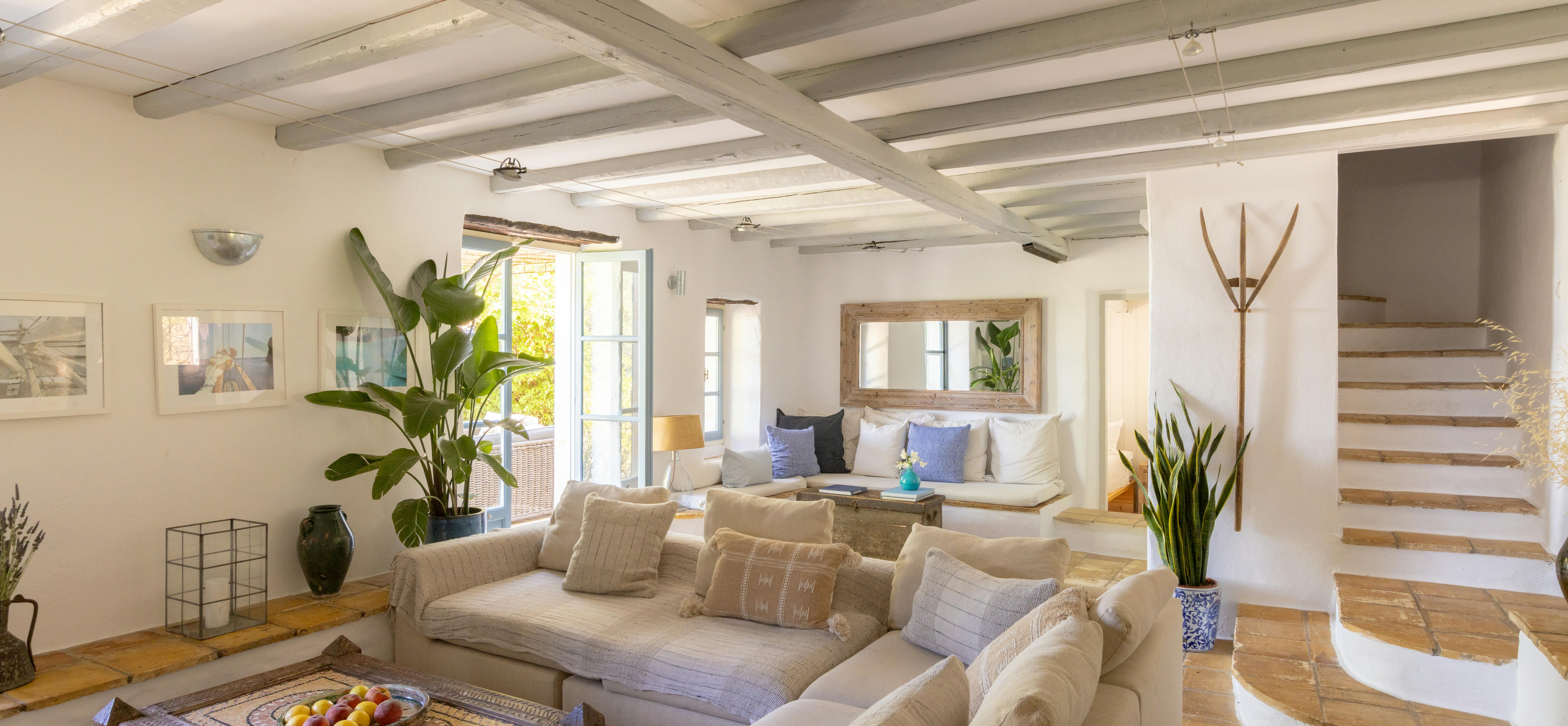 Open-concept living space with white beams, textured sectionals, carved coffee table, and floating stairs leading to upper level.
