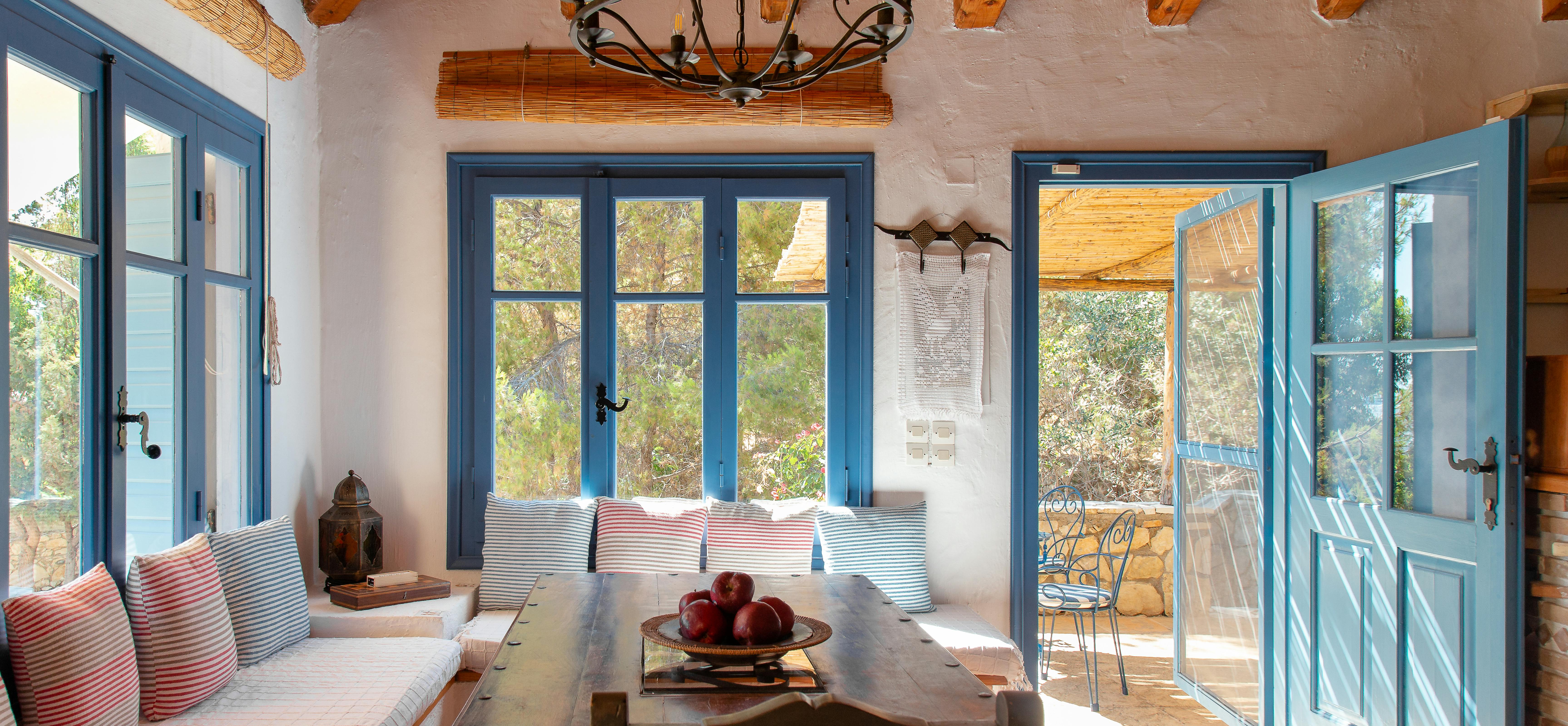 Rustic dining room with vaulted wood ceiling, long farm table, built-in bench seating with striped pillows, and blue French doors.