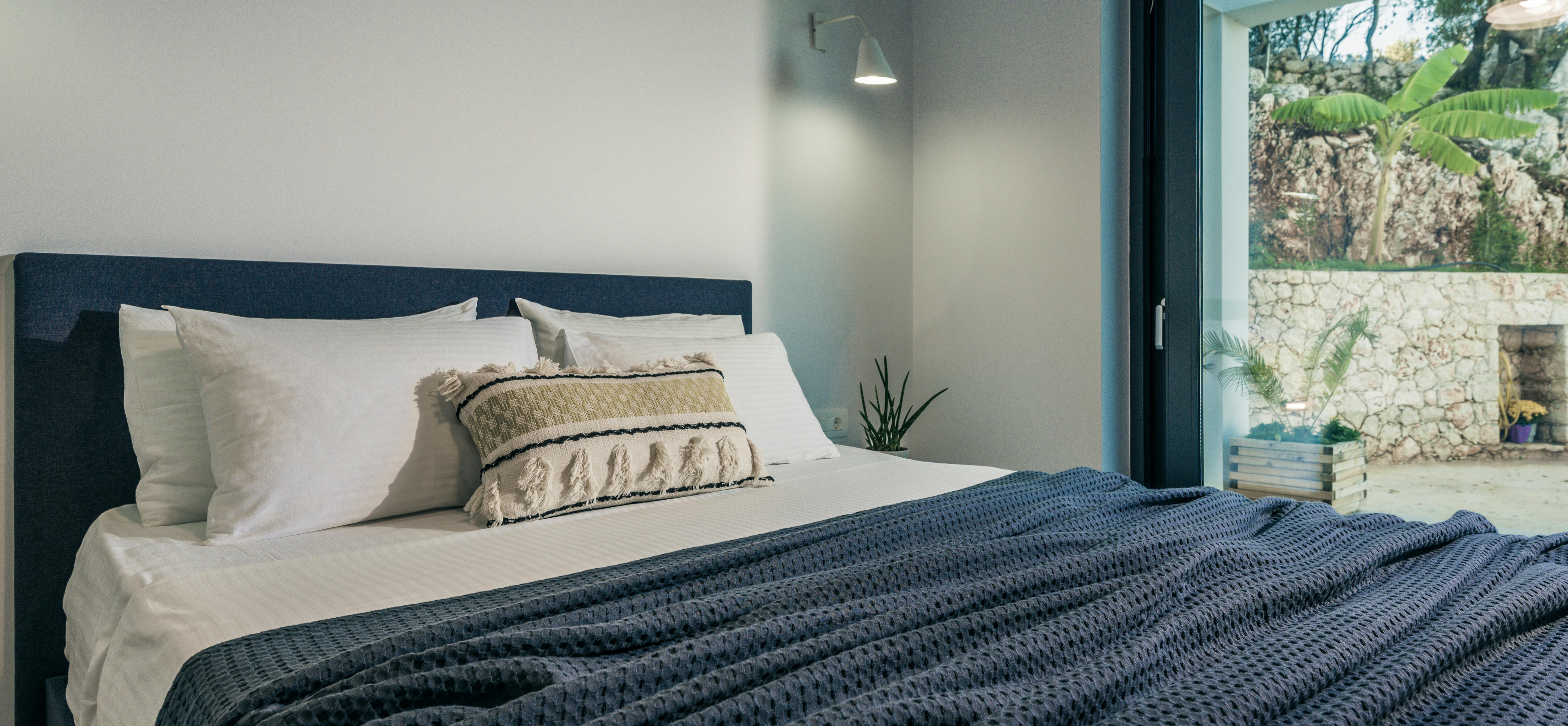 Minimalist bedroom with navy bed, textured blue throw, and doorway opening to tropical garden with stone retaining wall.