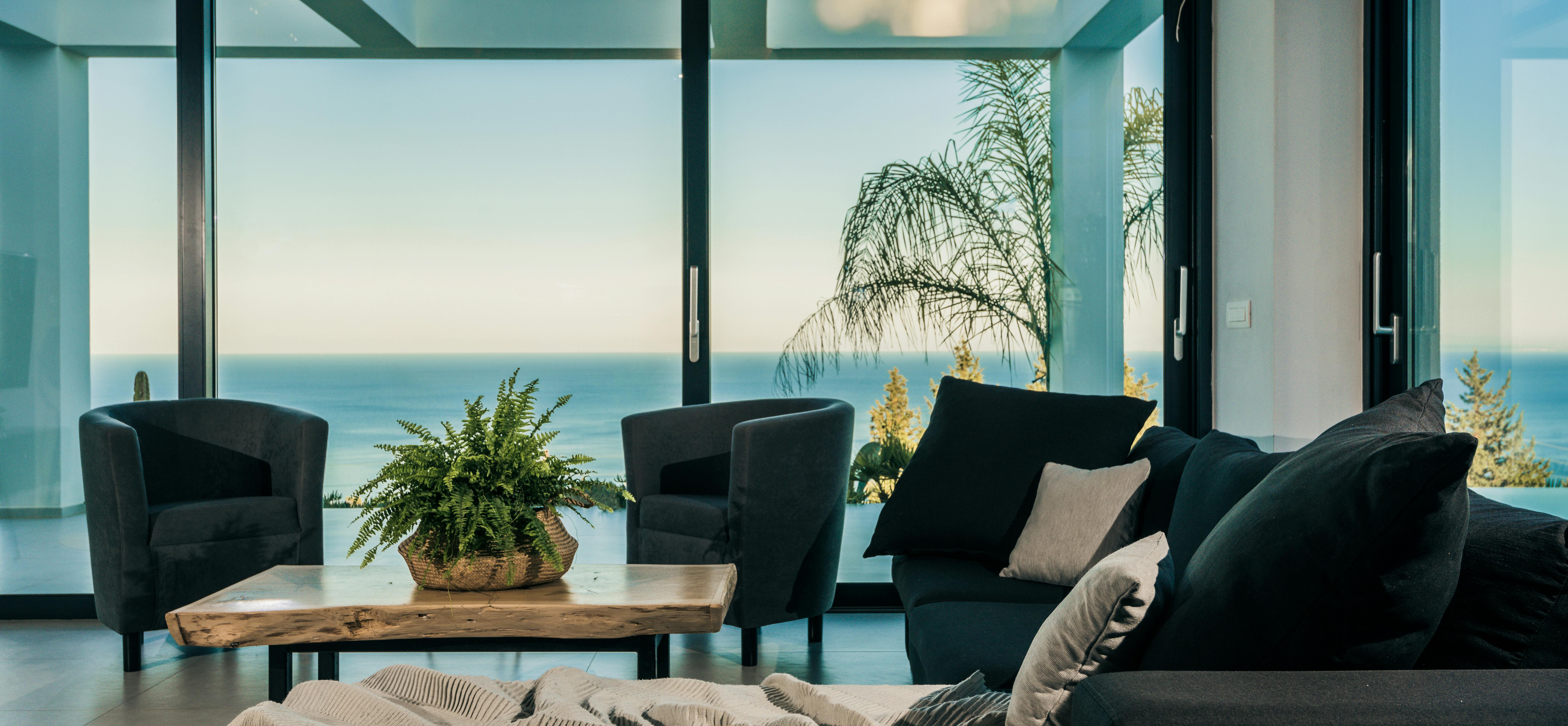 Contemporary lounge with black velvet seating, live-edge coffee table, and floor-to-ceiling glass framing palm trees and ocean horizon.