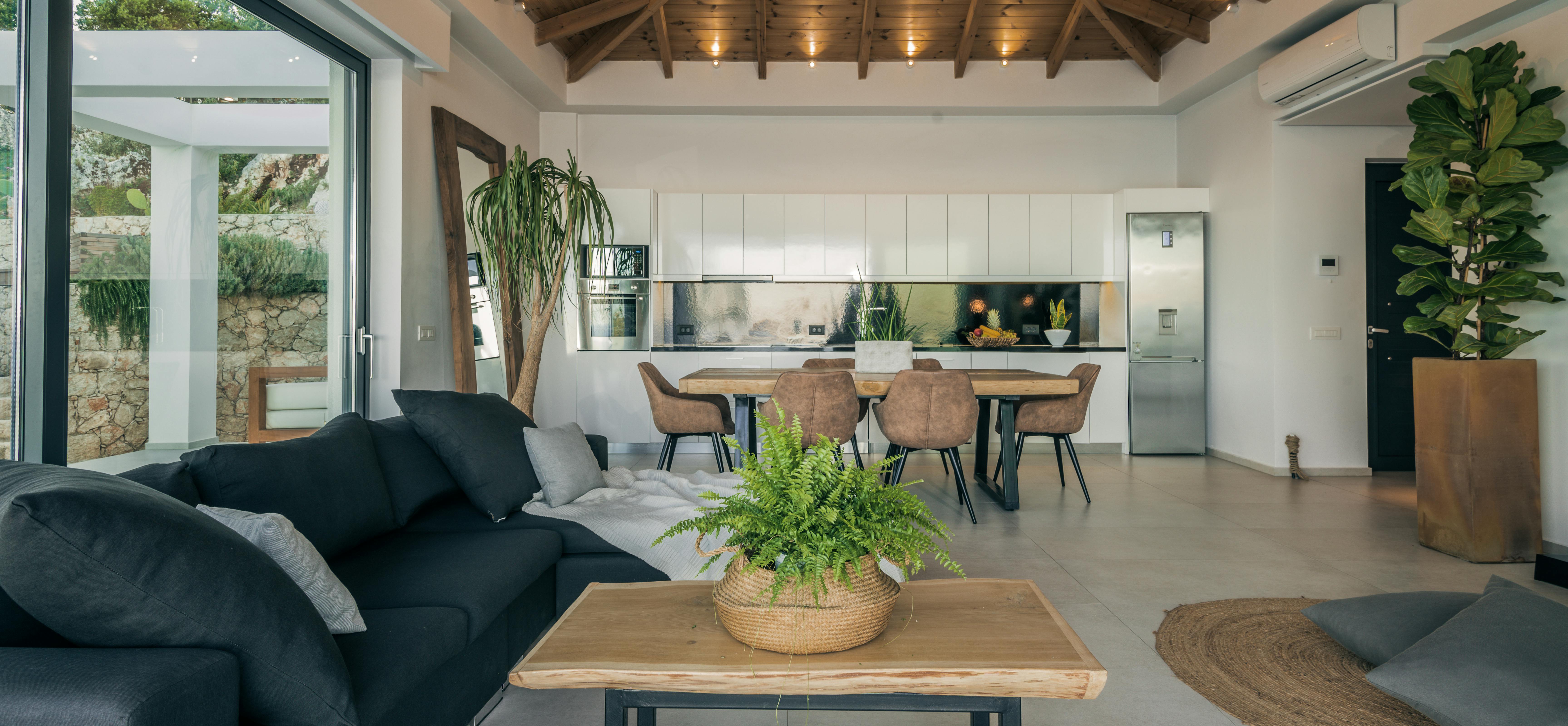 Open-plan living with vaulted wood ceiling, black sofas, live-edge dining table, and white kitchen beneath dramatic beam structure.