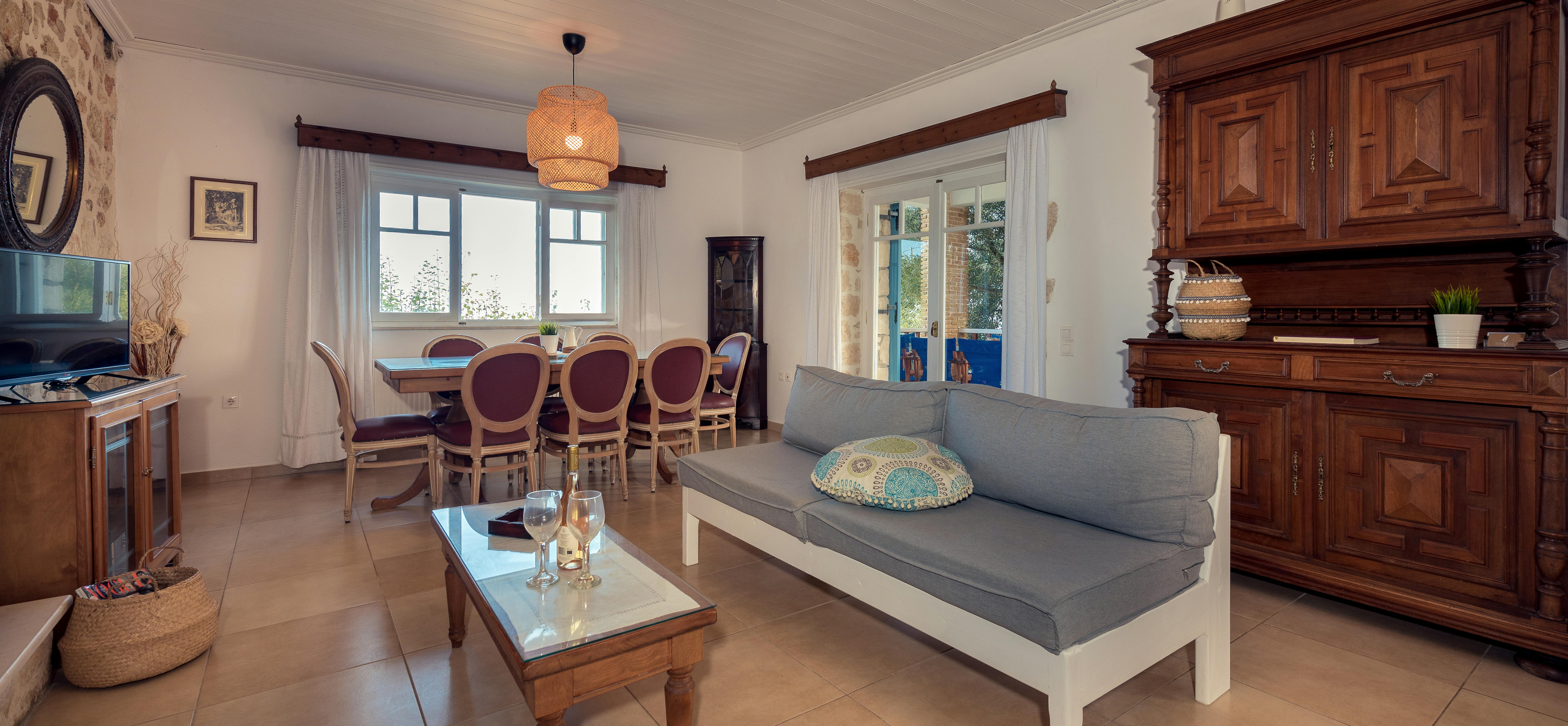 Living room with white built-in sofa, antique wooden hutch, purple upholstered dining chairs, and wicker pendant light.