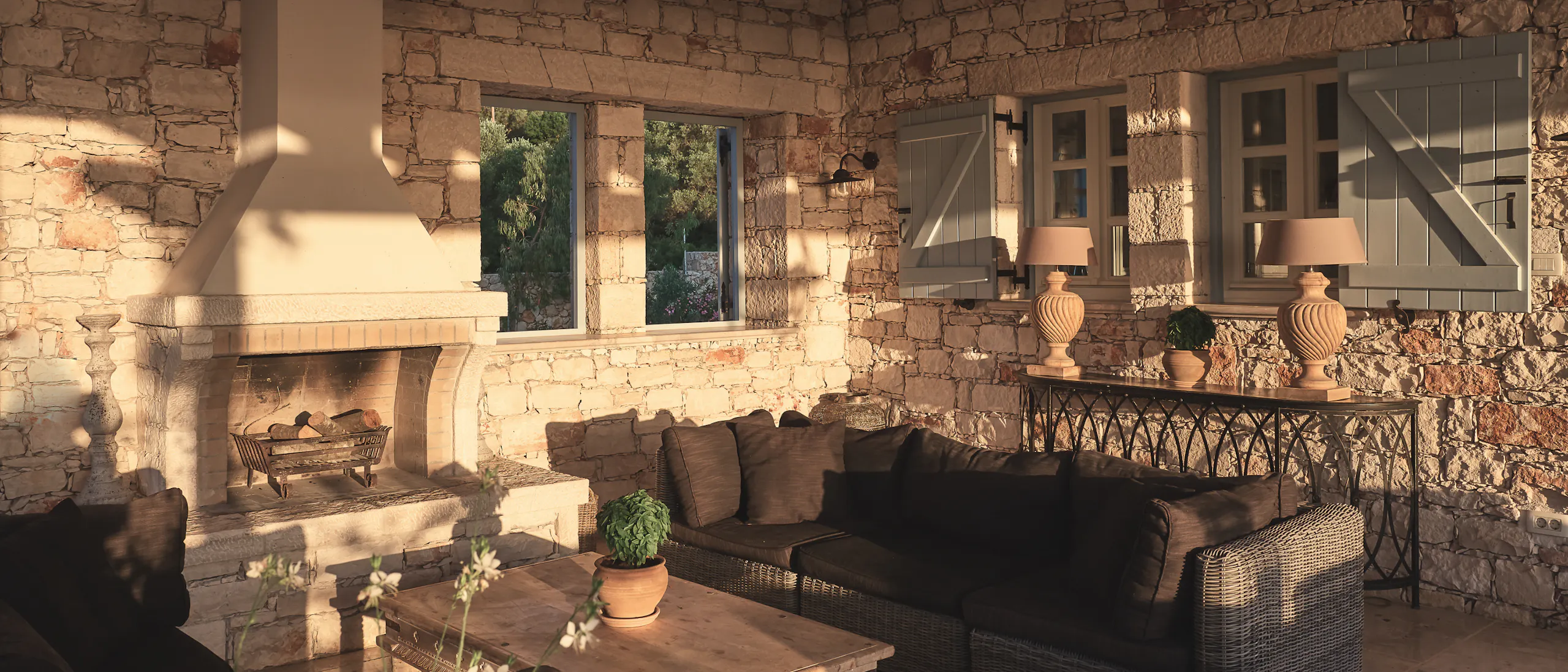 Covered outdoor living room with exposed stone walls, fireplace, and wicker furniture under vaulted ceiling.