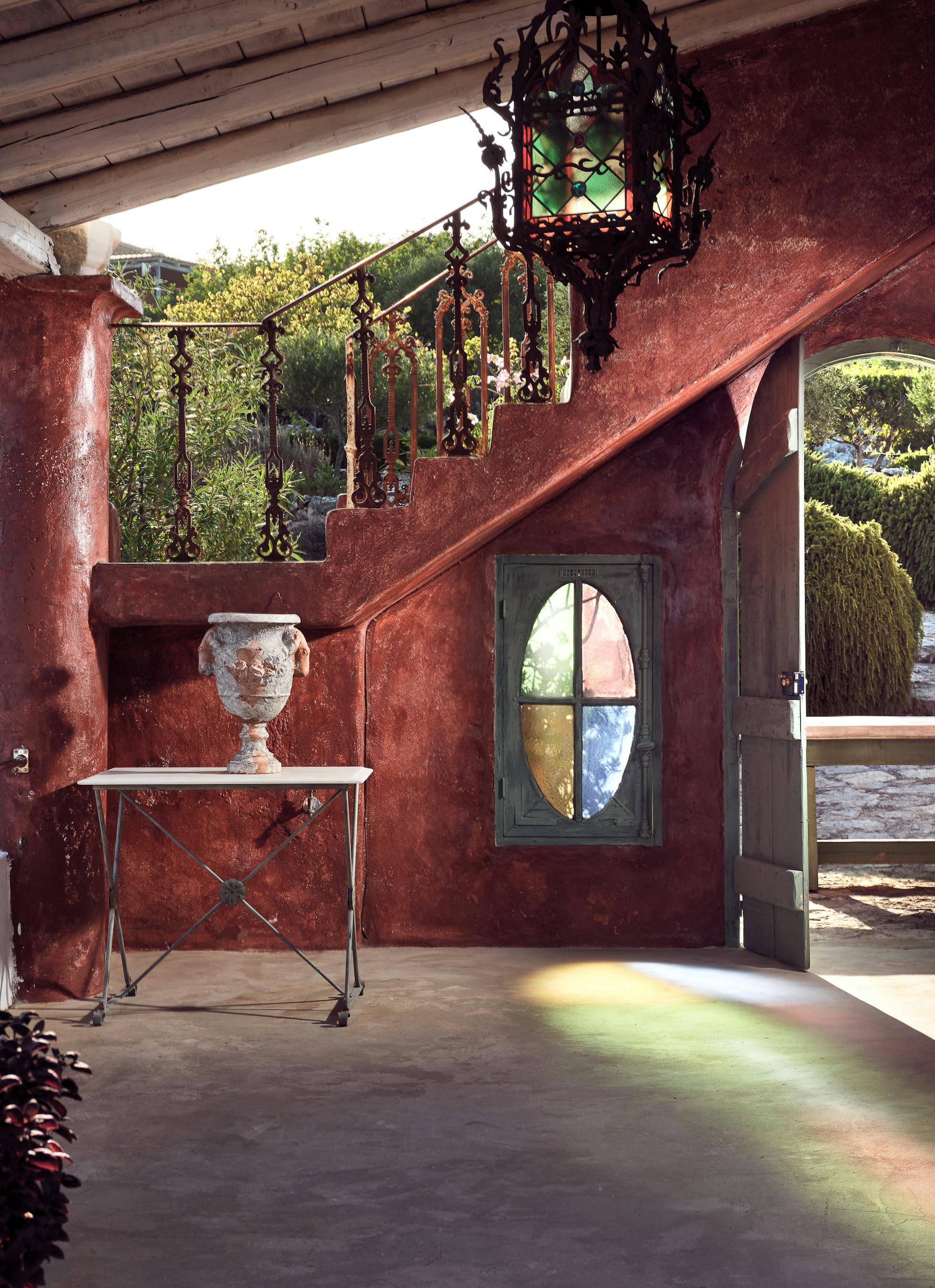 Dramatic covered entrance with rust-red walls, ornate Moroccan lantern, decorative door with stained glass oval, white console table, and carved details.