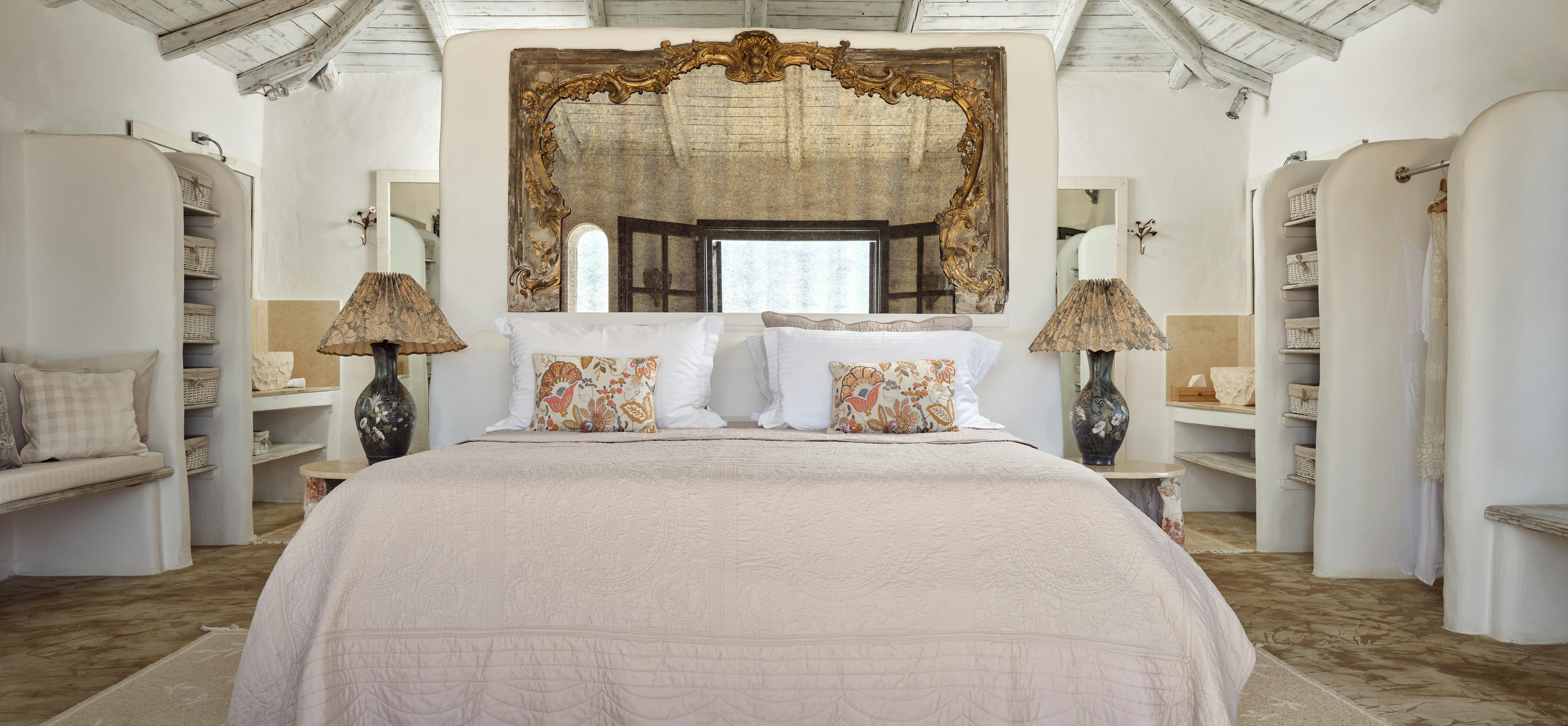 Grand bedroom with vaulted whitewashed wood ceiling, ornate gilded mirror headboard, built-in shelving alcoves, dark ceramic lamps with woven shades, and patterned pillows.
