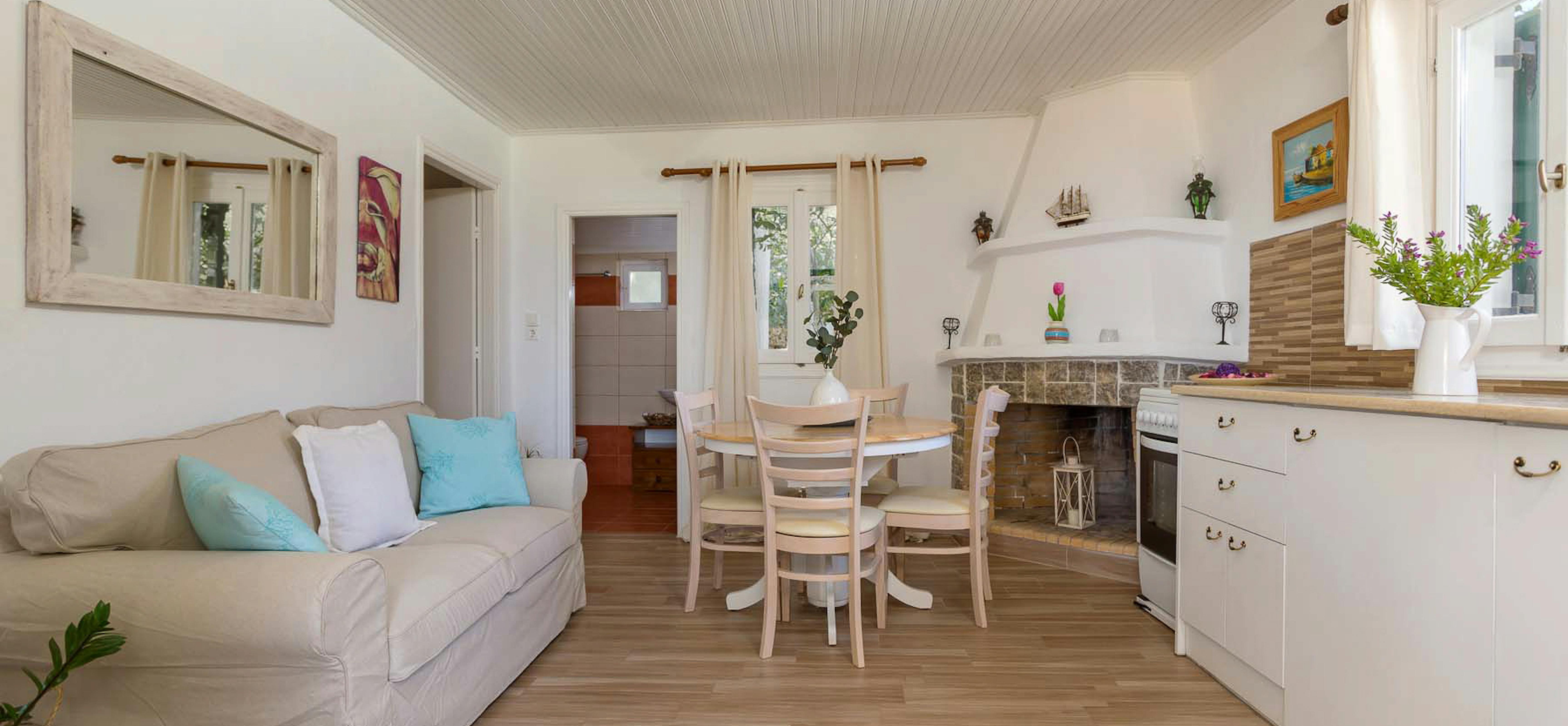 Coastal cottage living space with white kitchen, round dining table, beige sofa, and nautical decor.