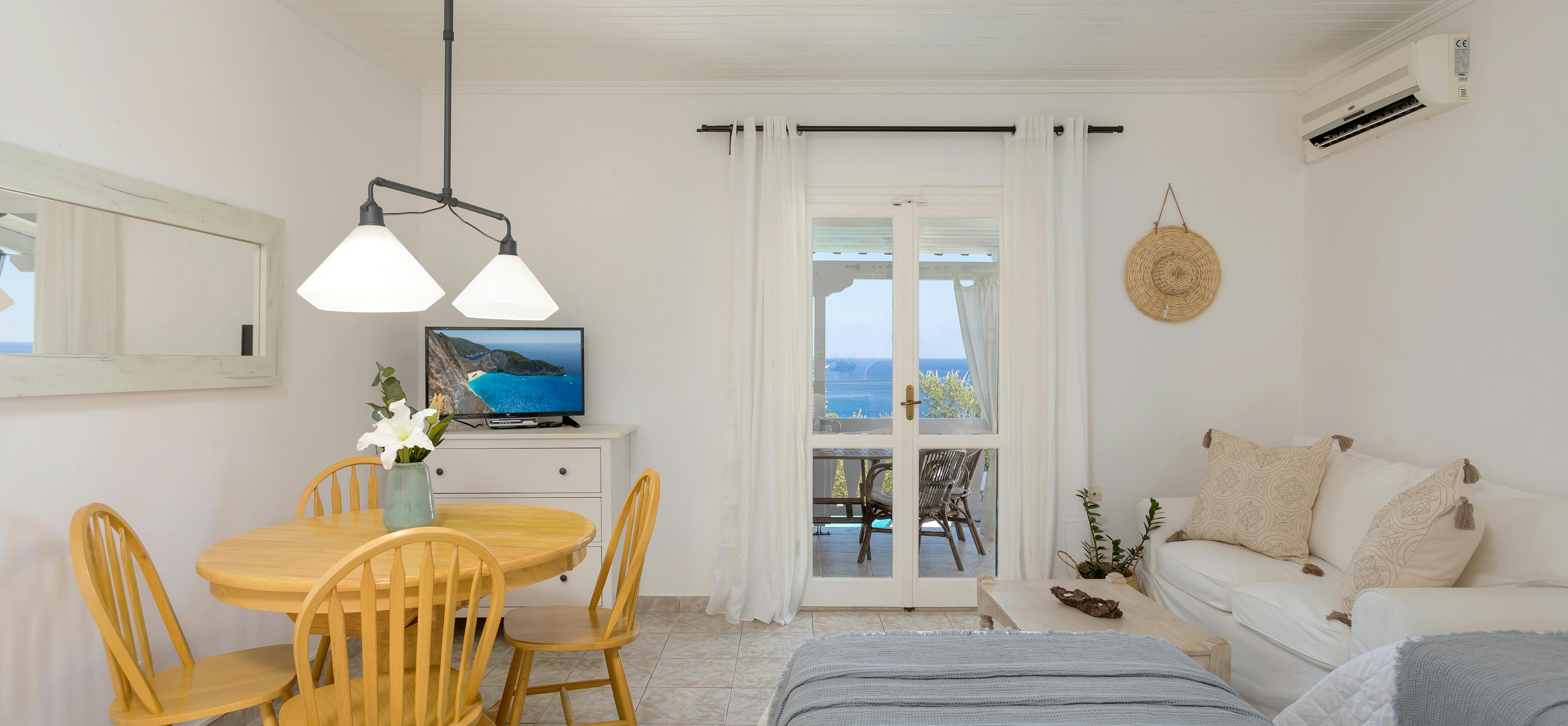 Studio interior with yellow dining set, twin beds with grey throws, and patio doors to balcony.