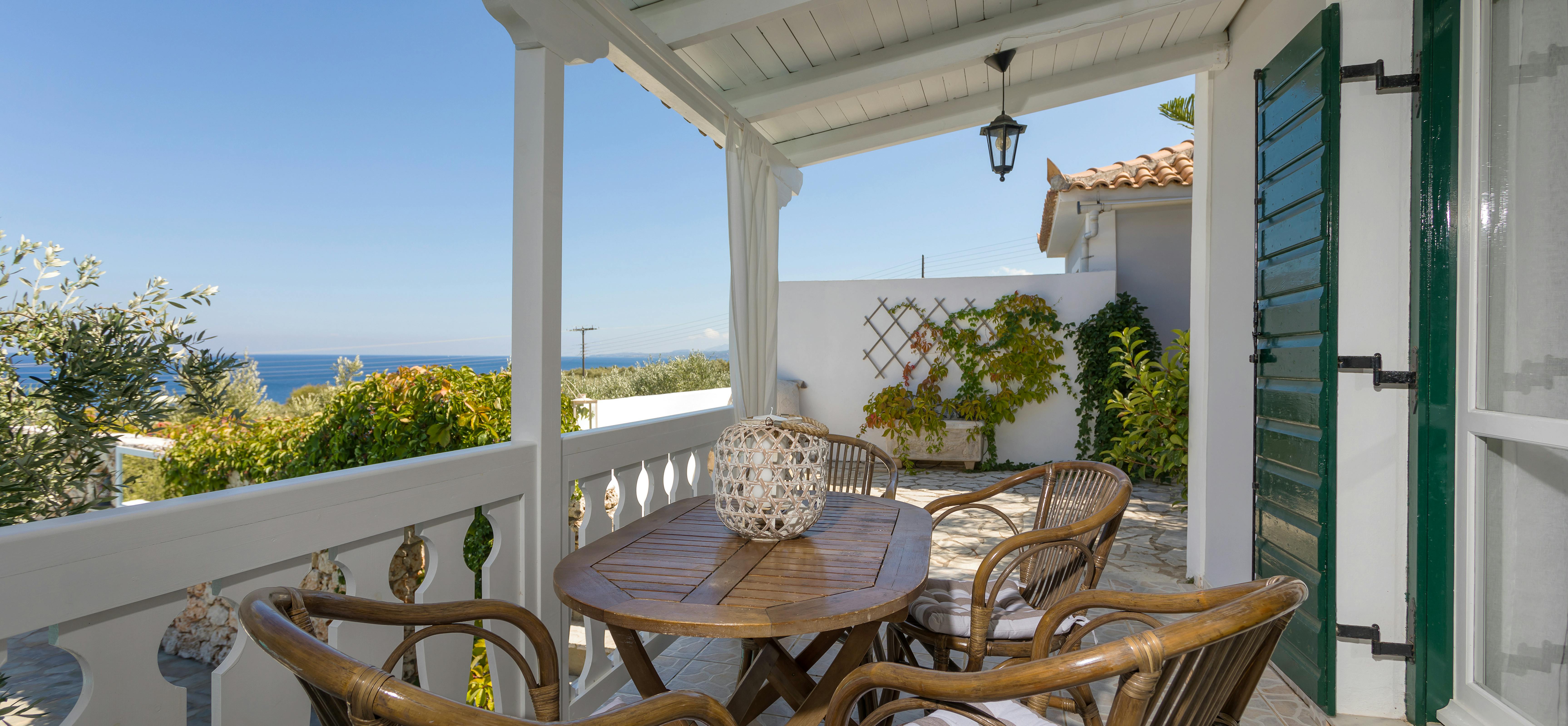 Covered terrace with wicker dining furniture, white balustrade, and panoramic coastal views.