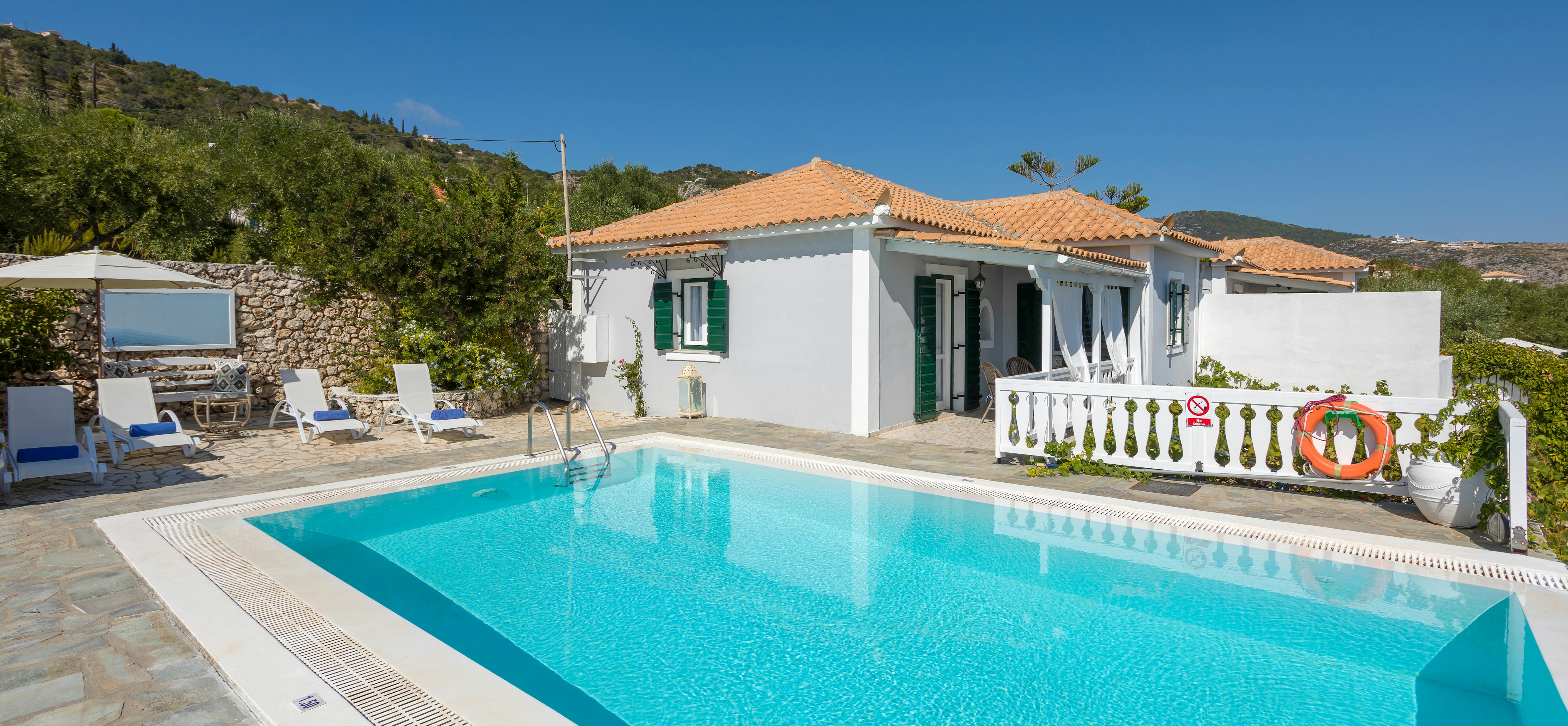 Mediterranean villa with swimming pool, white loungers, covered terrace, green shutters, and hillside setting.