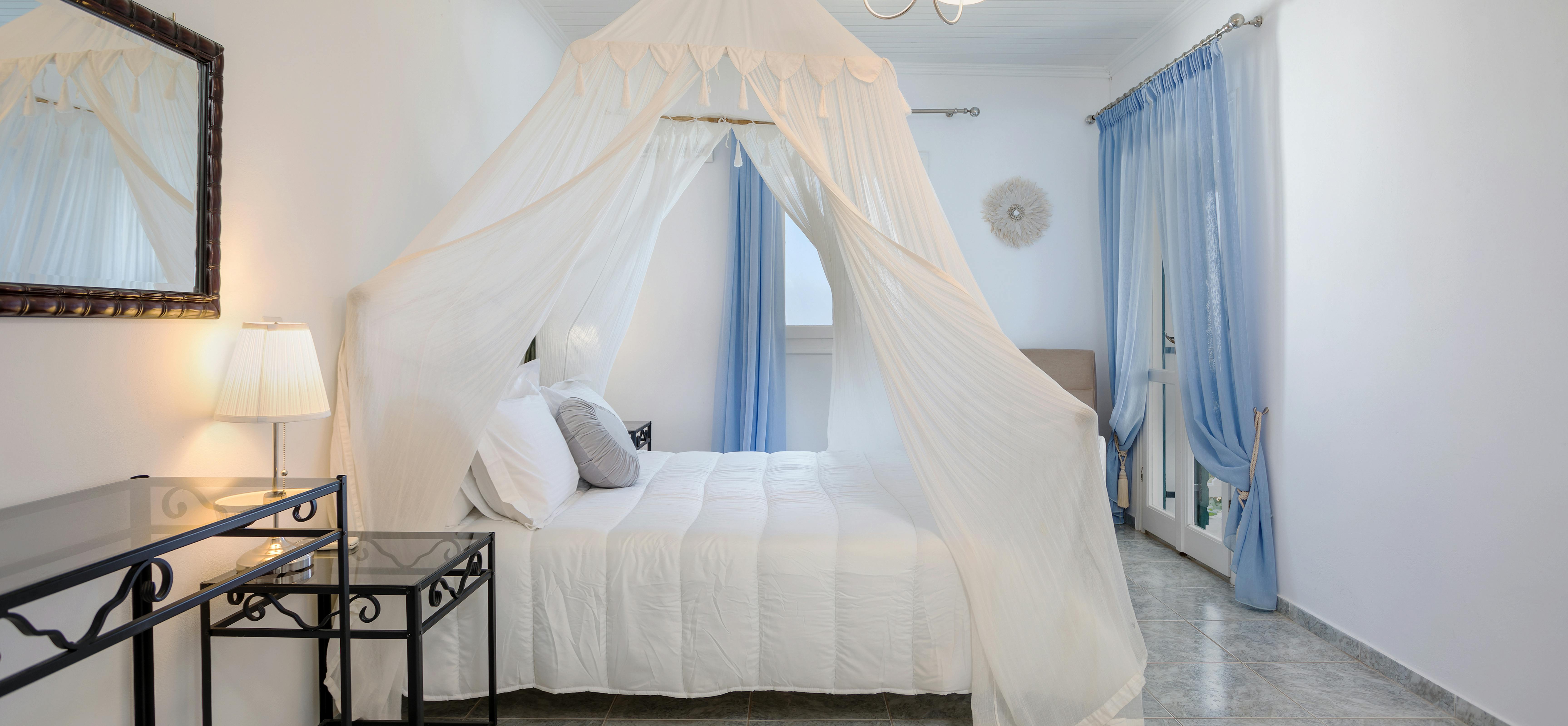 Romantic bedroom with white canopy bed, mosquito netting, blue curtains, and nightstands.