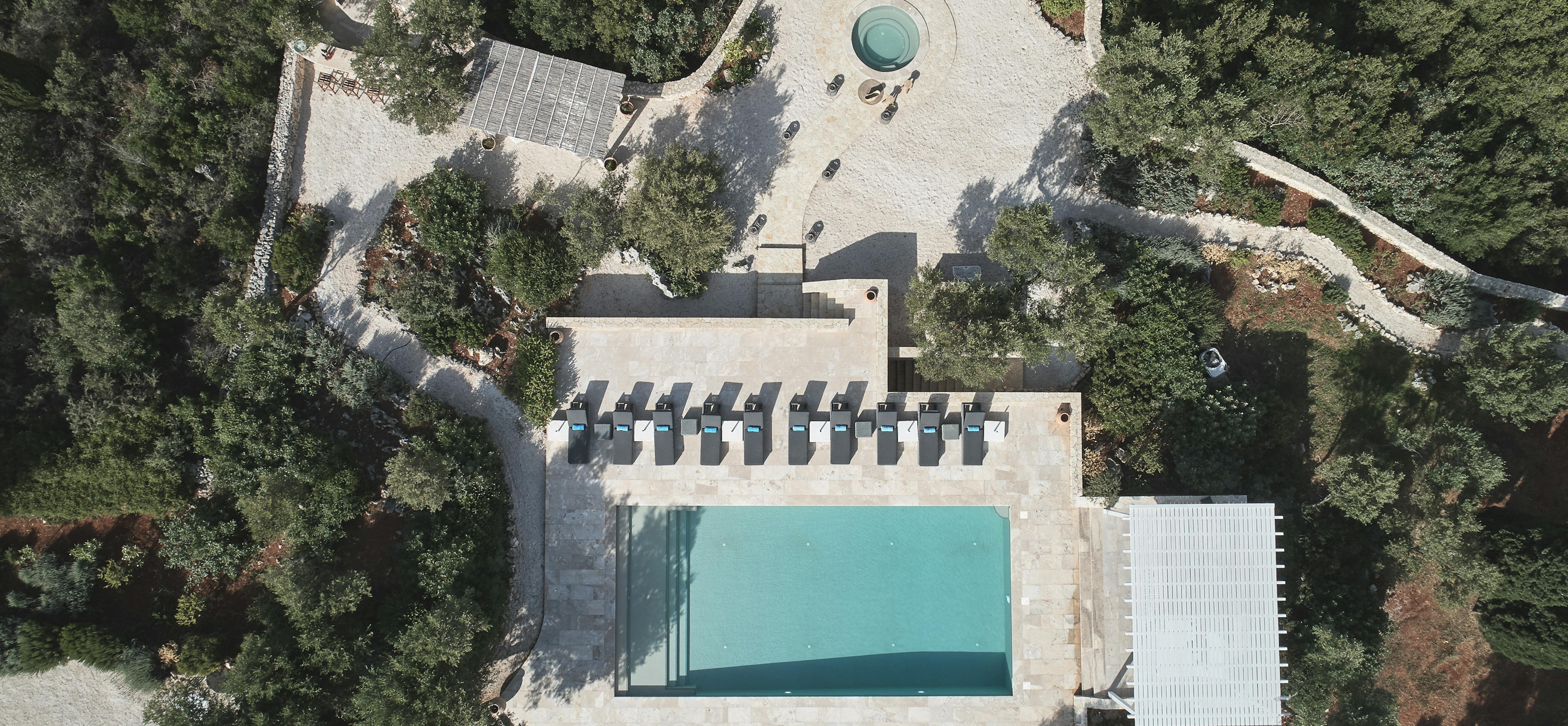 Aerial view of pool deck with loungers, white pergola, and circular hot tub surrounded by olive groves.