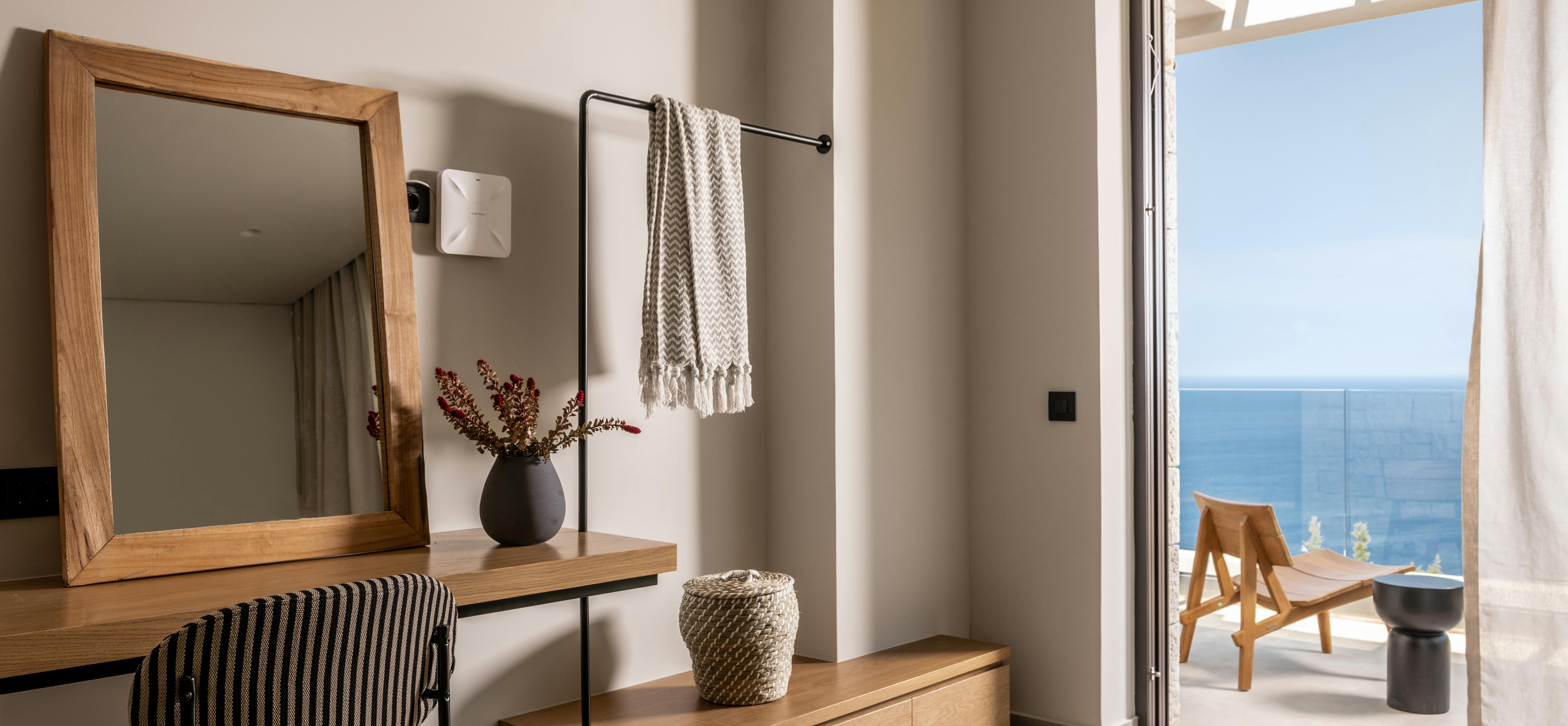 An interior dressing area with modern furnishings and a square mirror looks out through an open doorway toward the pool and ocean terrace.