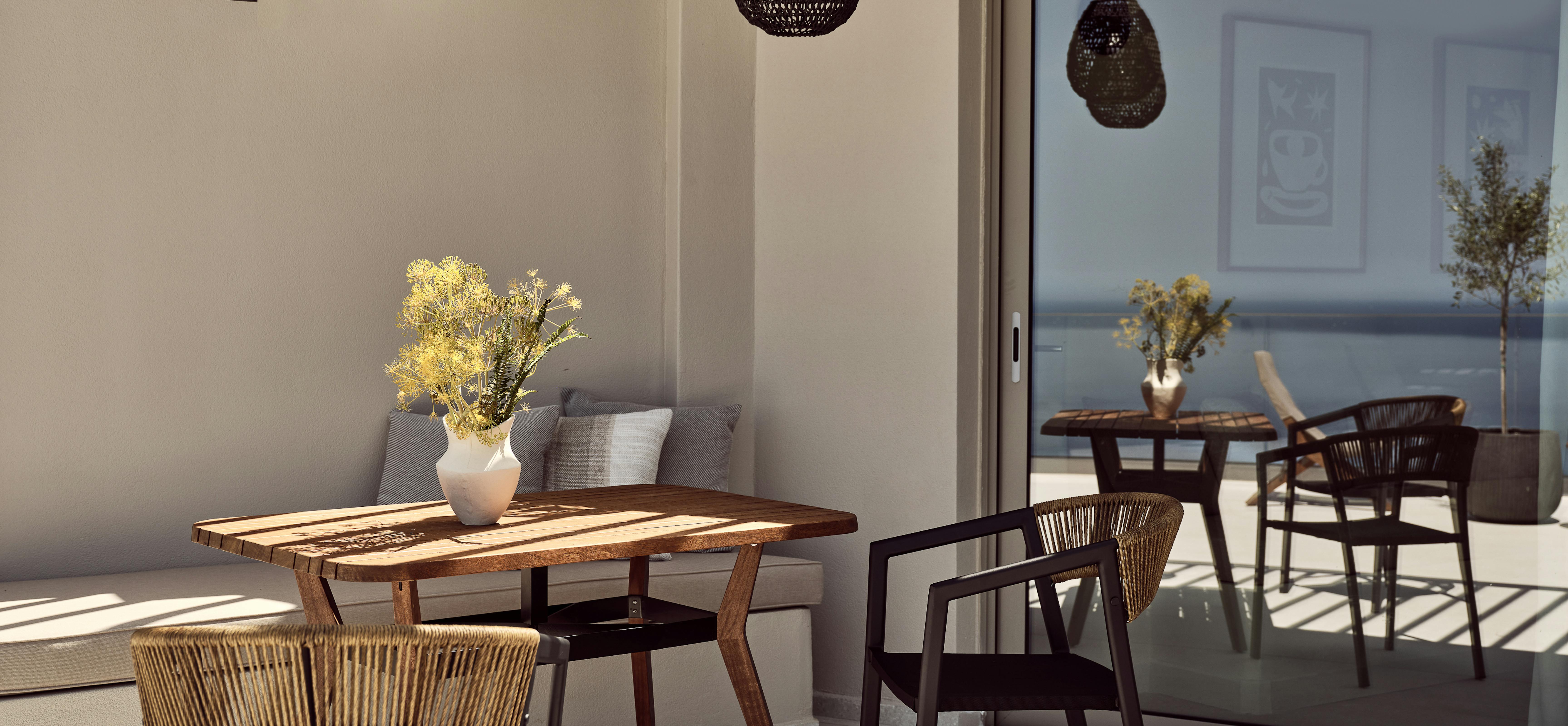 A covered terrace dining area with a live-edge wooden table, woven chairs, built-in bench seating, and pendant lights overlooking the sea.
