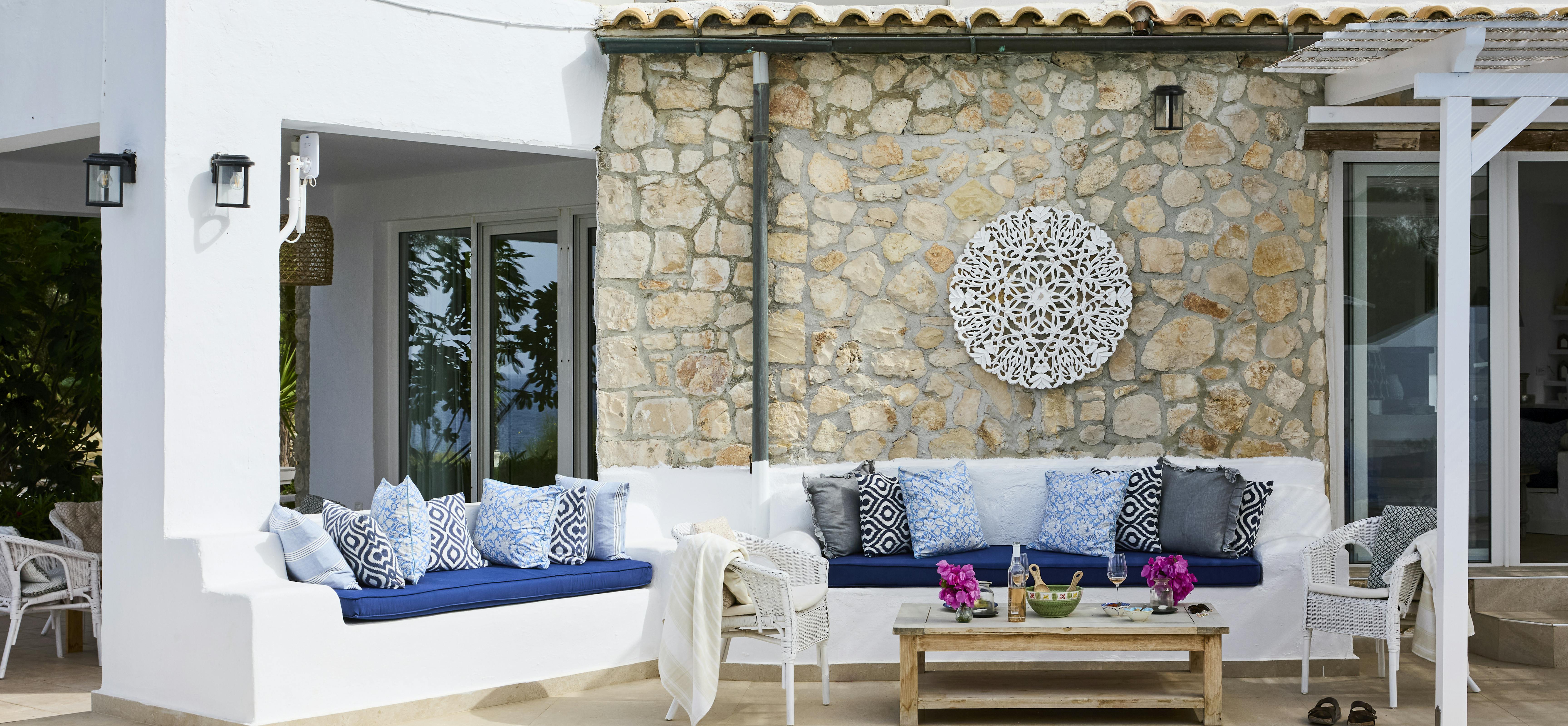 Mediterranean terrace with white built-in benches topped with navy and blue patterned cushions, stone wall backdrop, and decorative circular medallion.