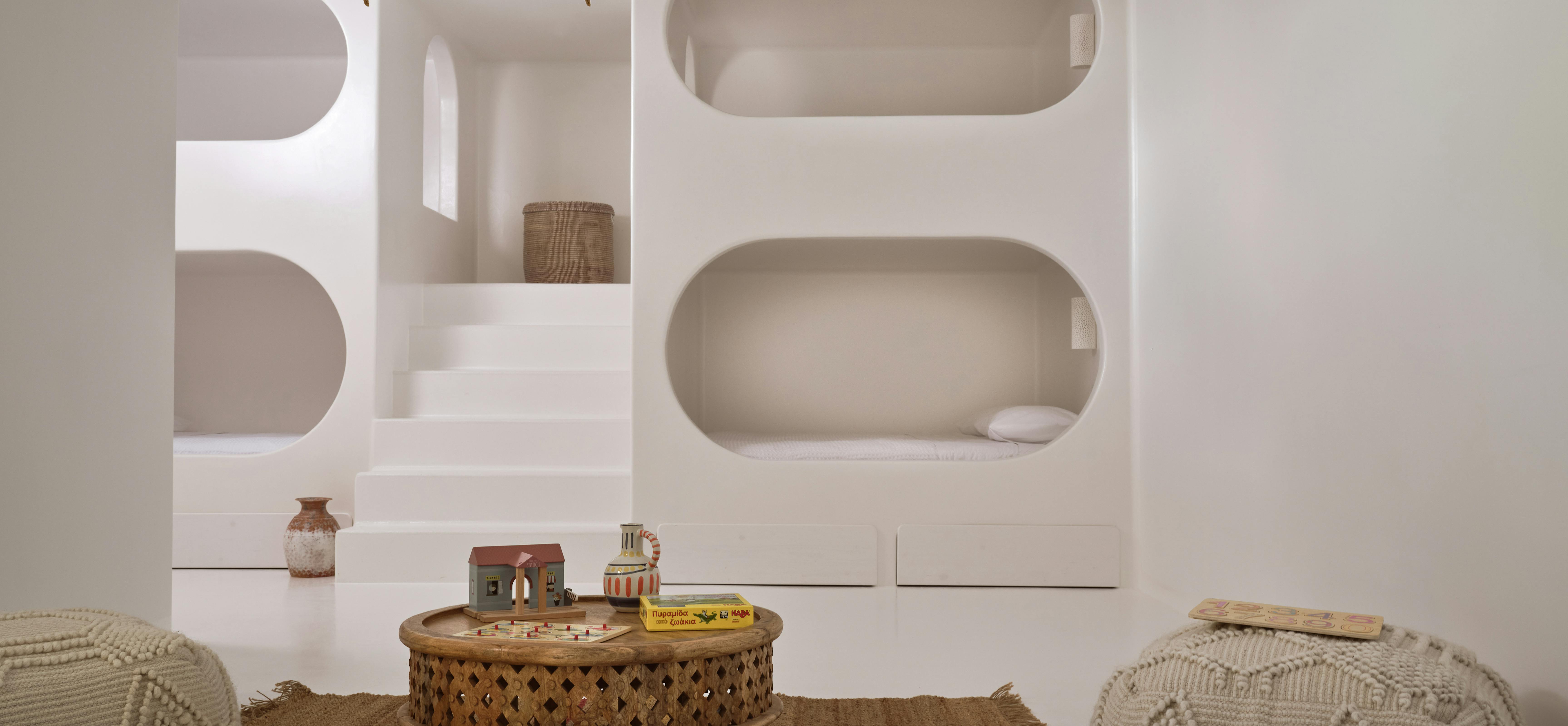 White minimalist bedroom with curved build in bunk beds, woven poufs, and decorative fish-shaped wall hangings.