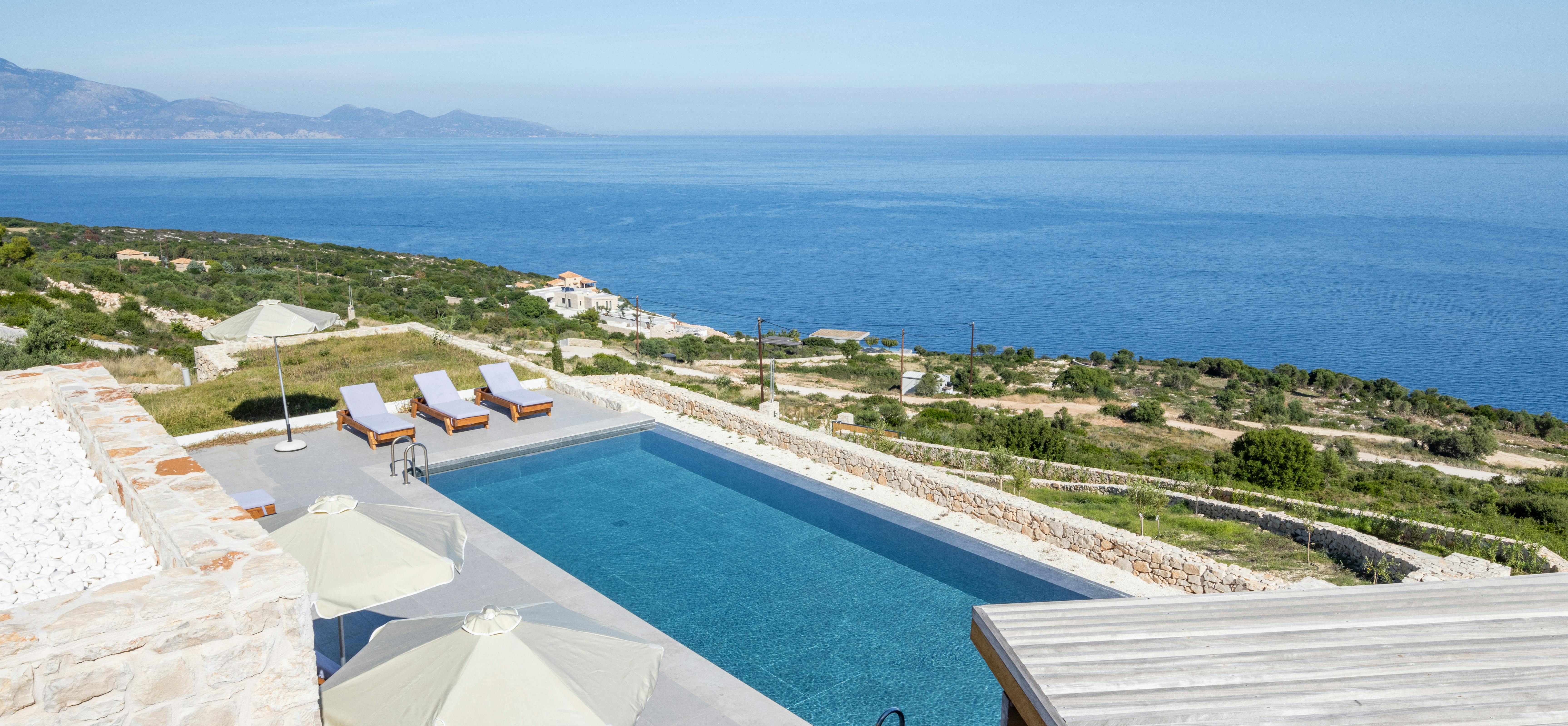 Infinity pool overlooking terraced hillside vineyards and blue sea with mountains in distance.