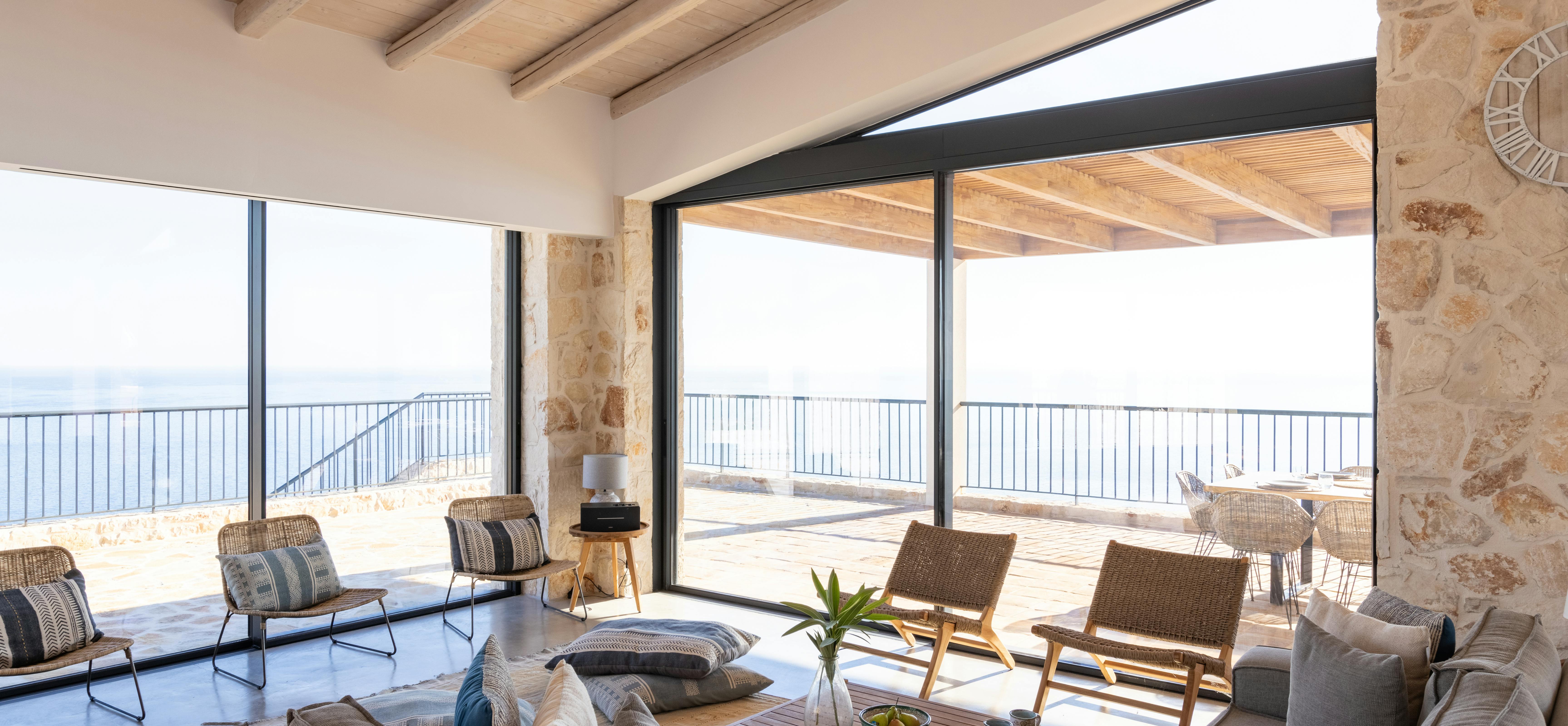 Living room with floor-to-ceiling glass doors opening to covered terrace with panoramic coastal views.
