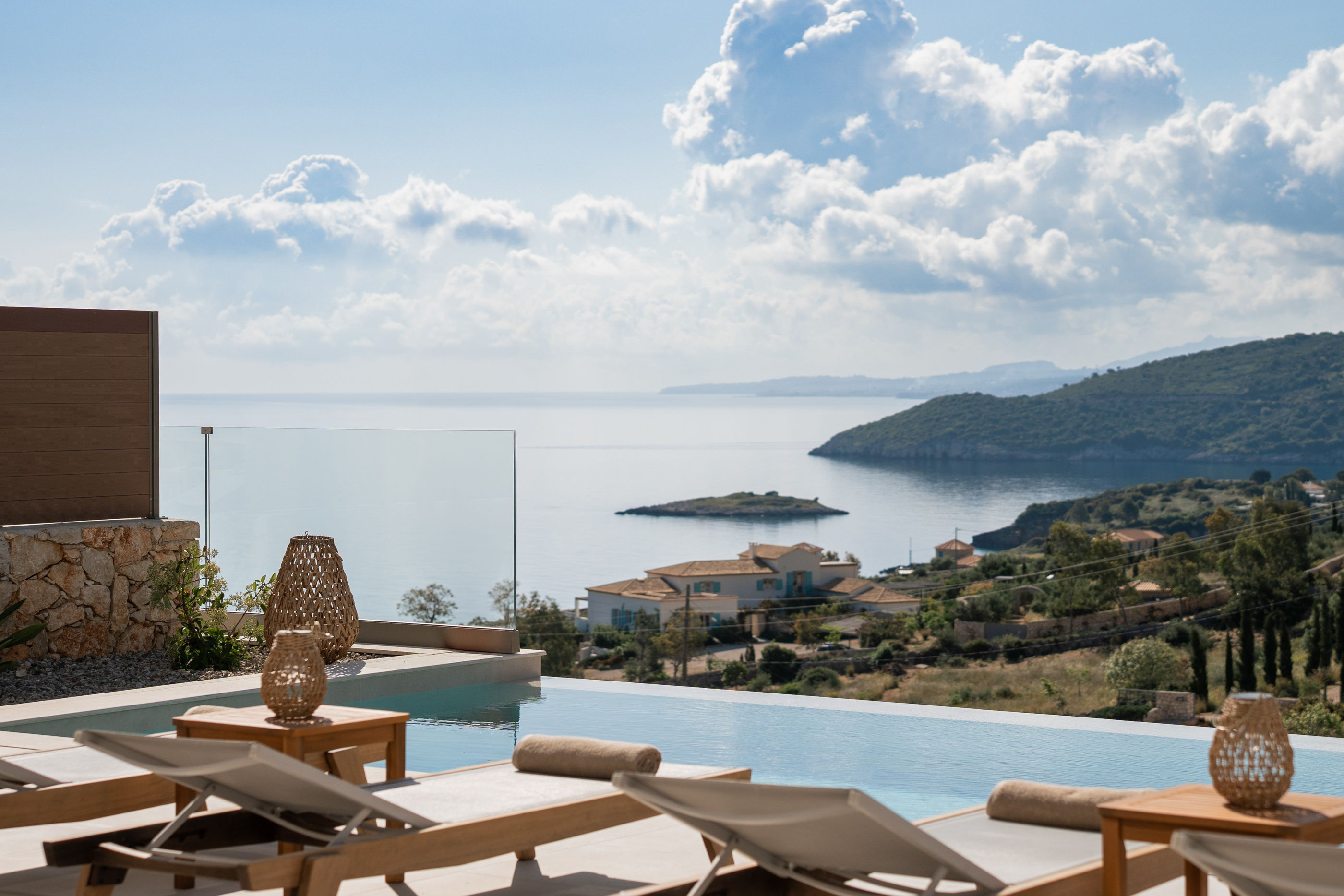 Wooden lounge chairs on terrace overlooking calm sea with dramatic cloudy sky at sunset.